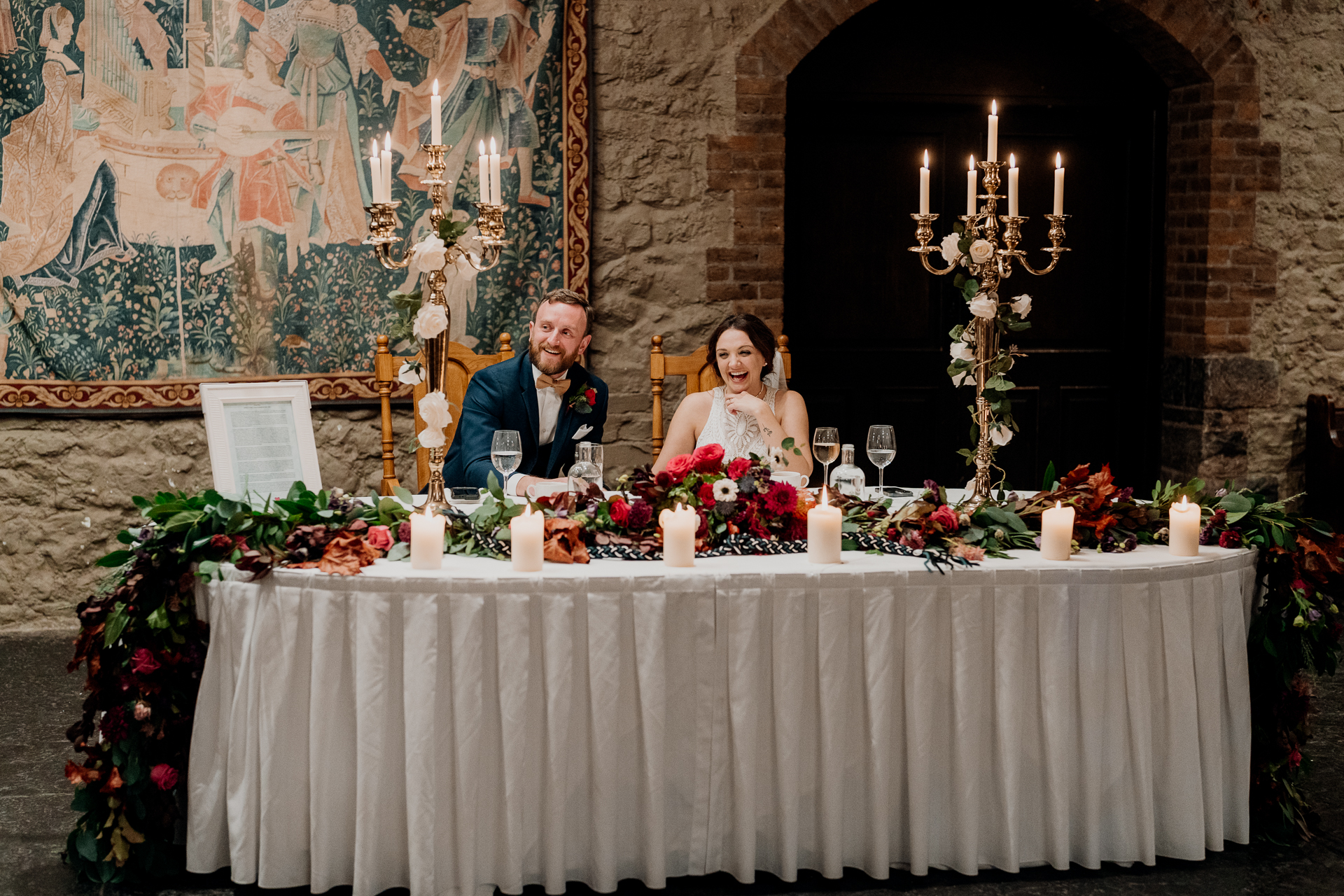 A bride and groom sitting at a table with a bouquet of flowers