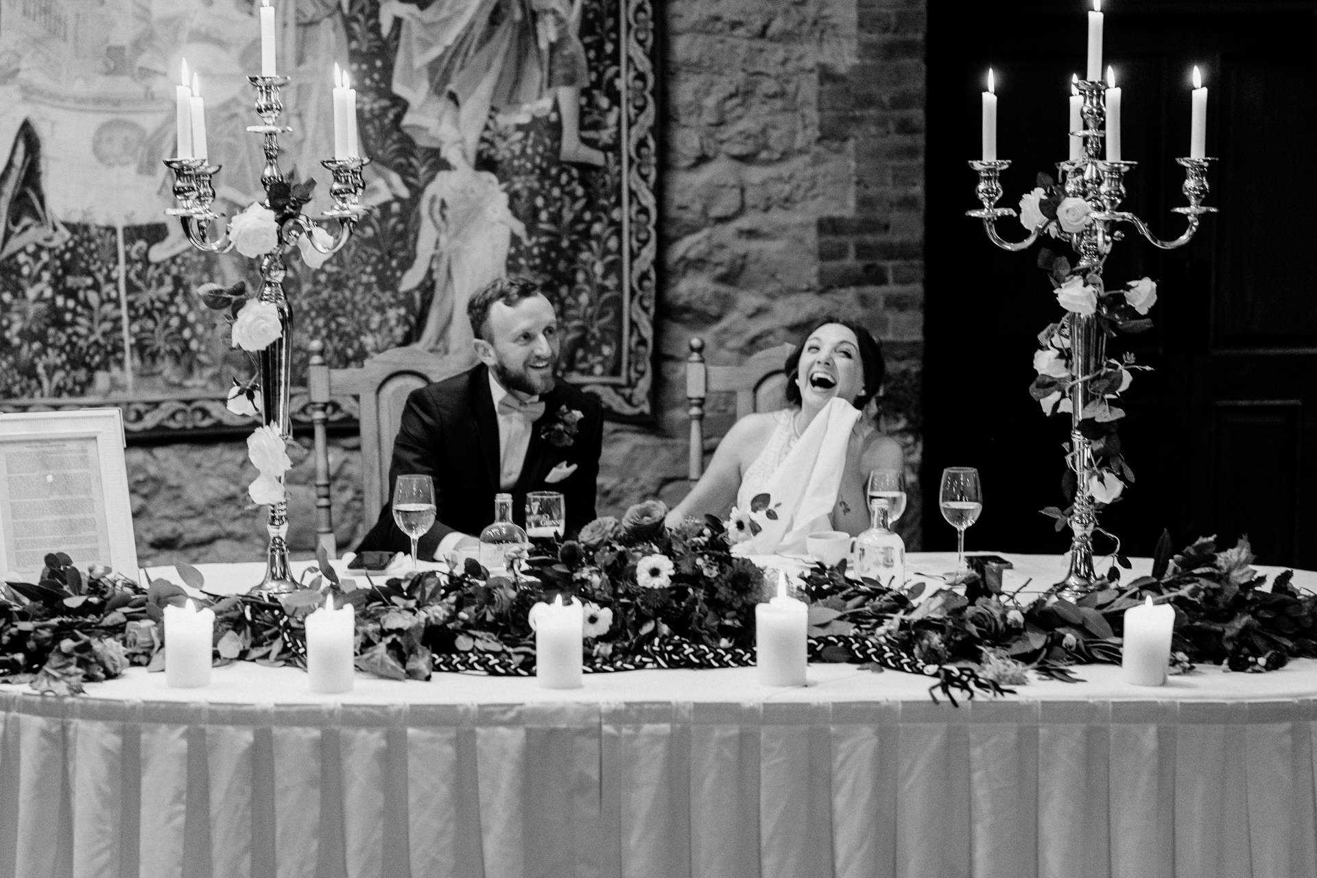 A bride and groom sitting at a table with candles and flowers