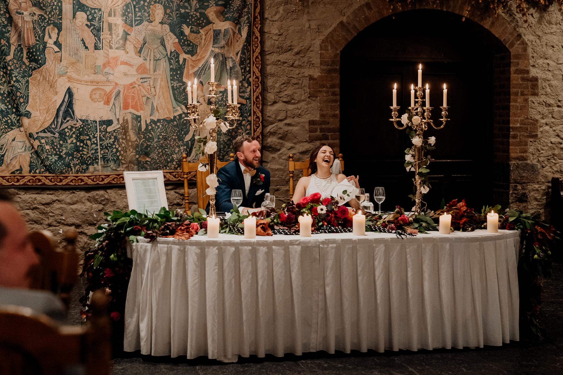 A bride and groom sitting at a table with a bouquet of flowers