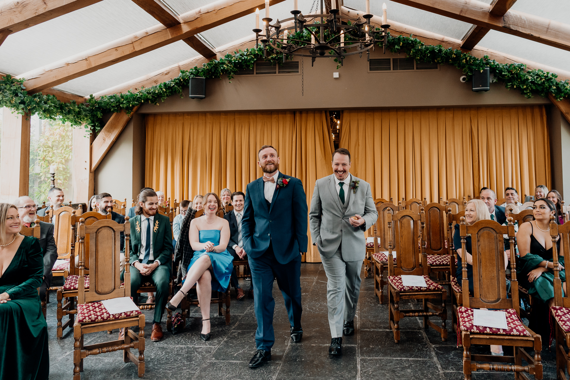 A couple of men walking down a hall with a group of people sitting in chairs