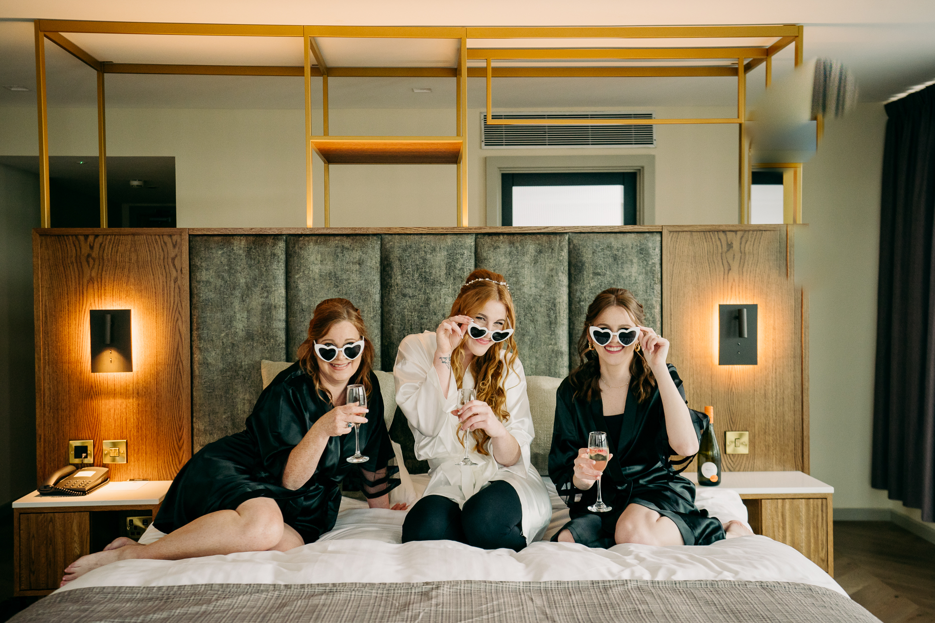 A group of women wearing sunglasses and sitting on a bed