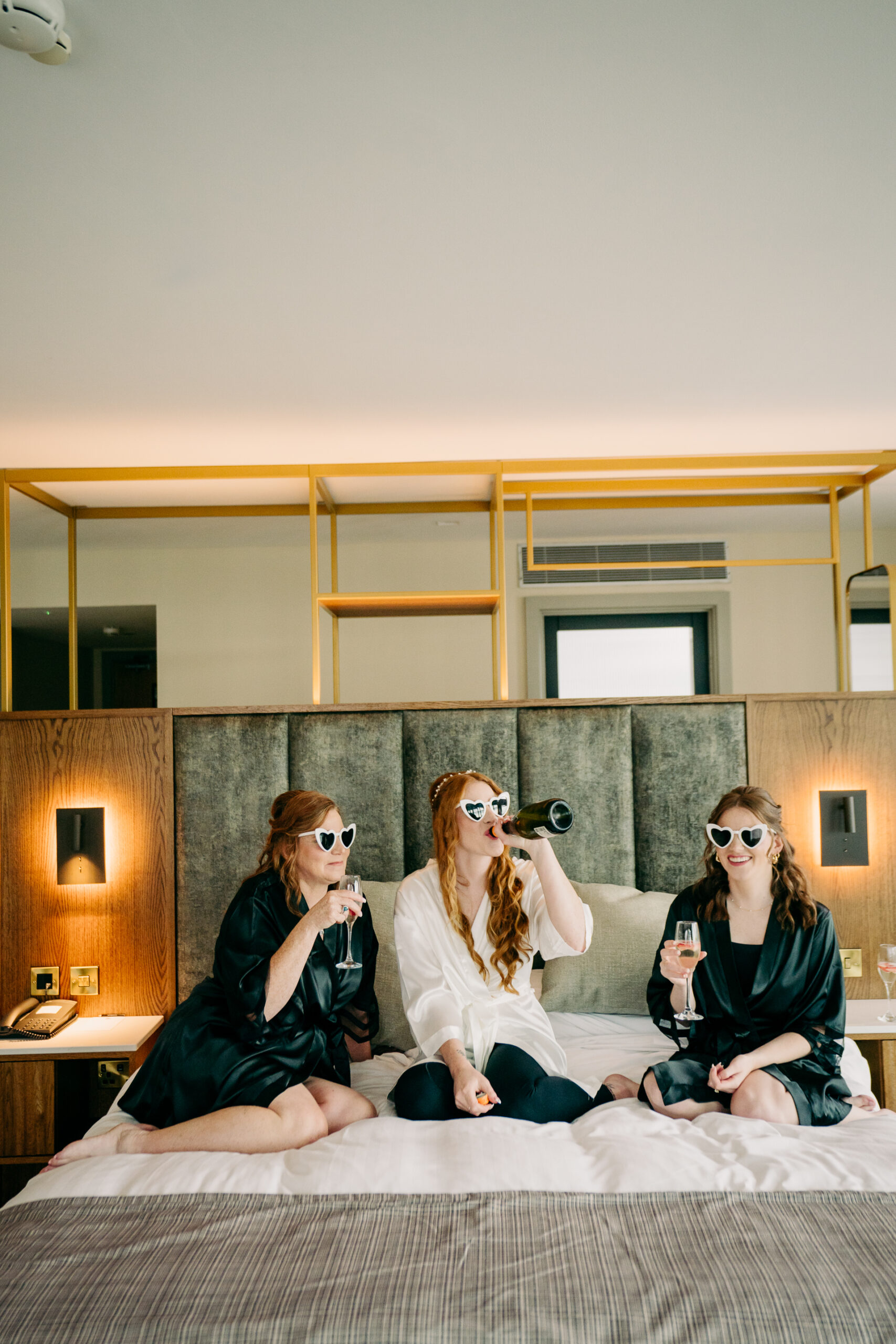 A group of women sitting on a bed with glasses and holding guns