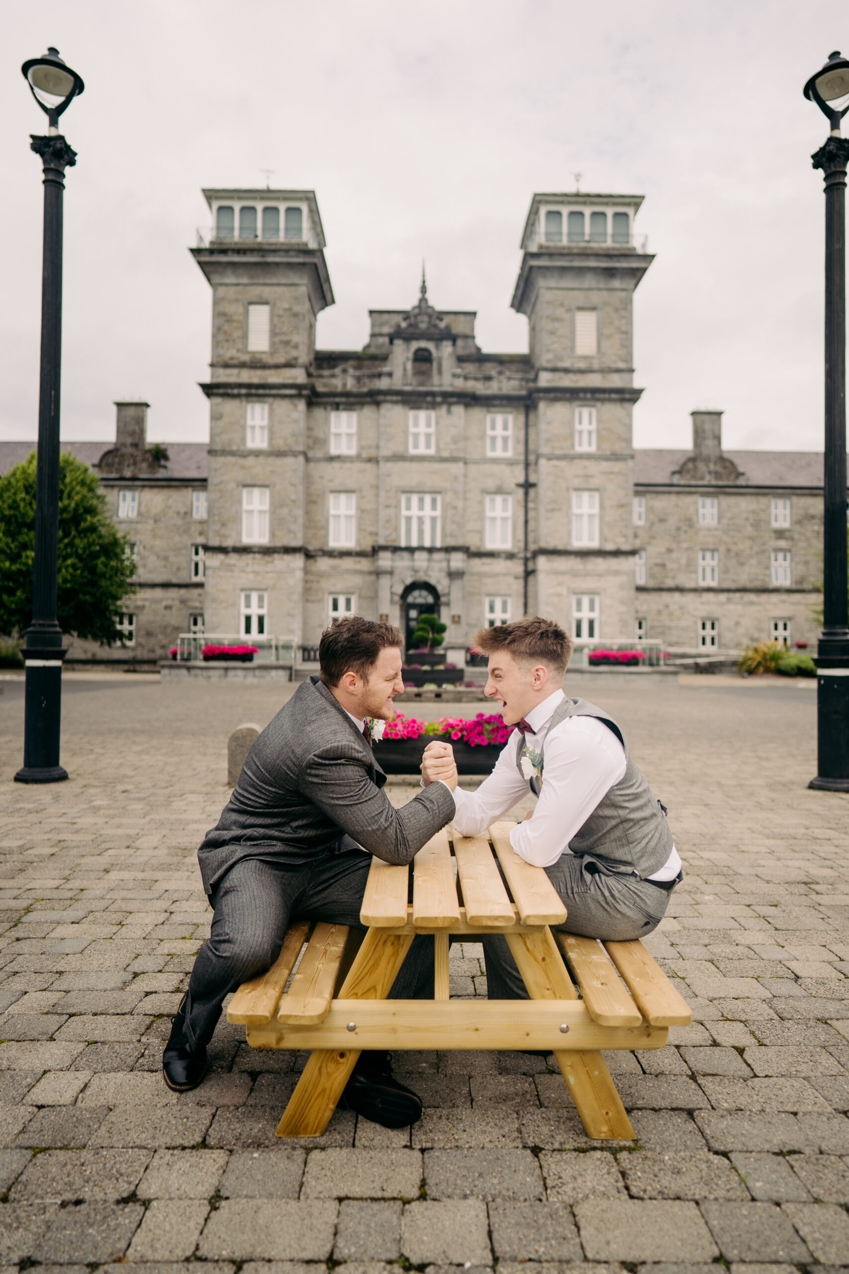 A couple of men sitting on a bench with flowers in front of a building