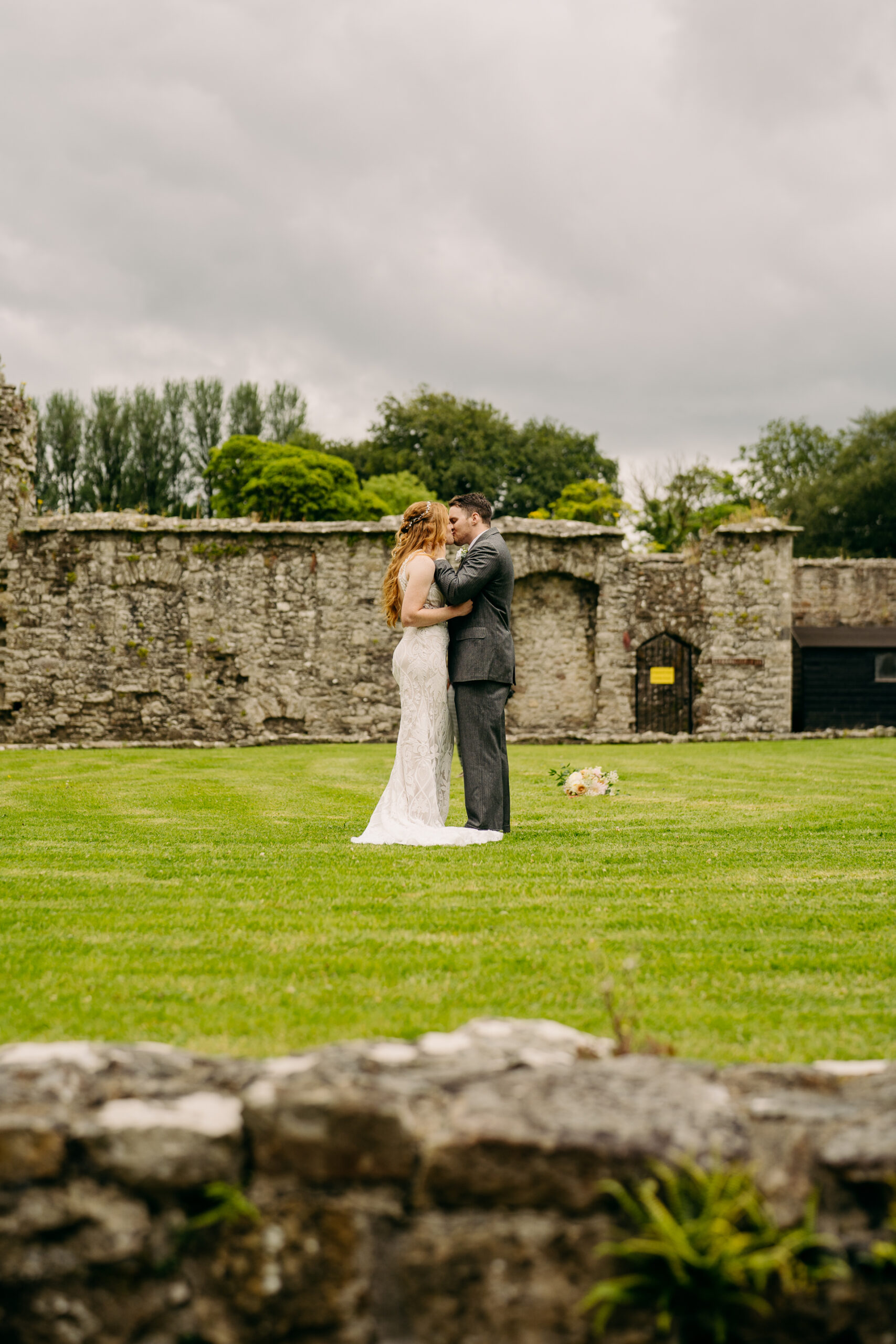 A man and woman kissing in front of a stone wall and grass