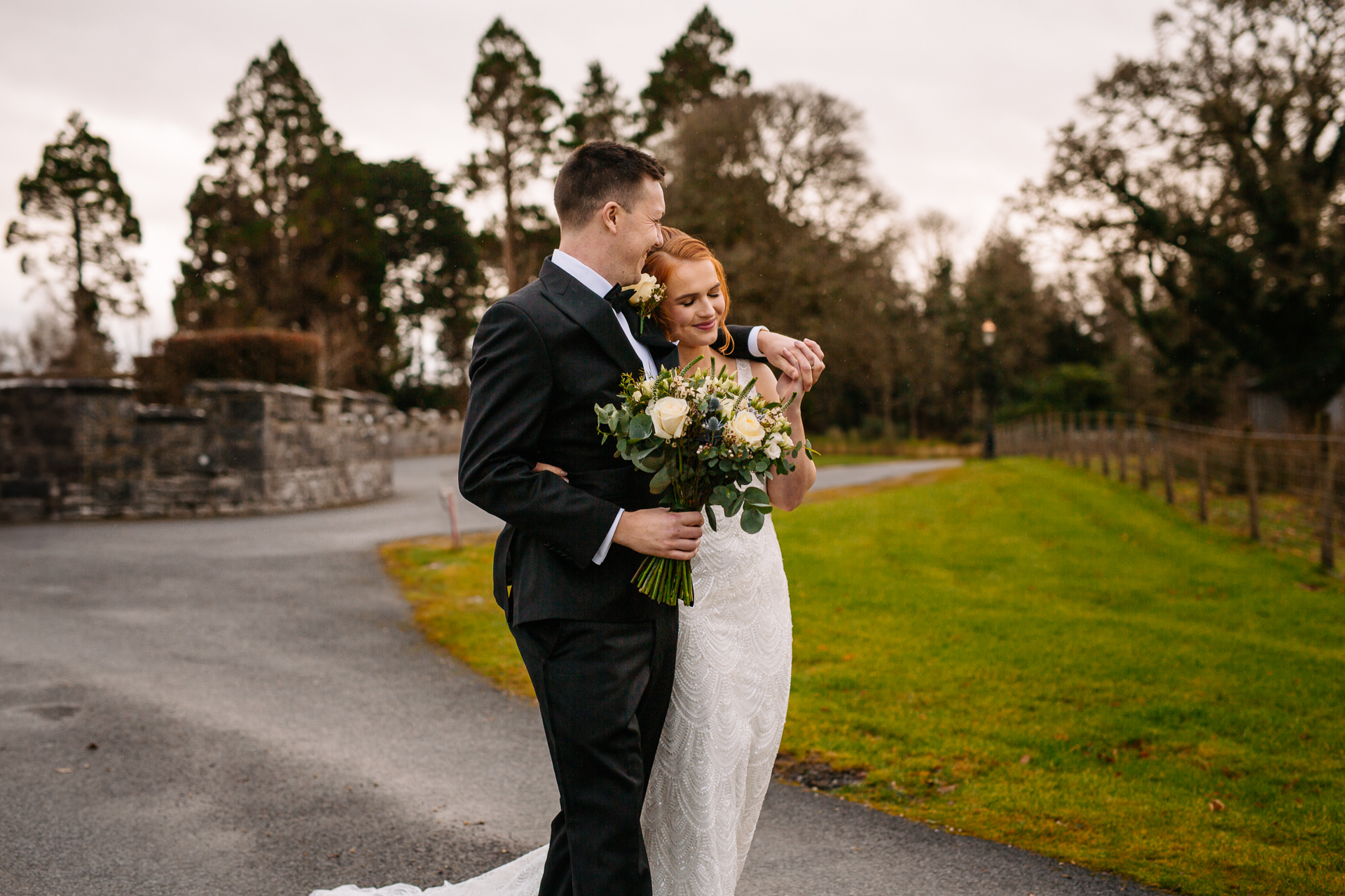 A man and woman kissing on a road with grass and trees