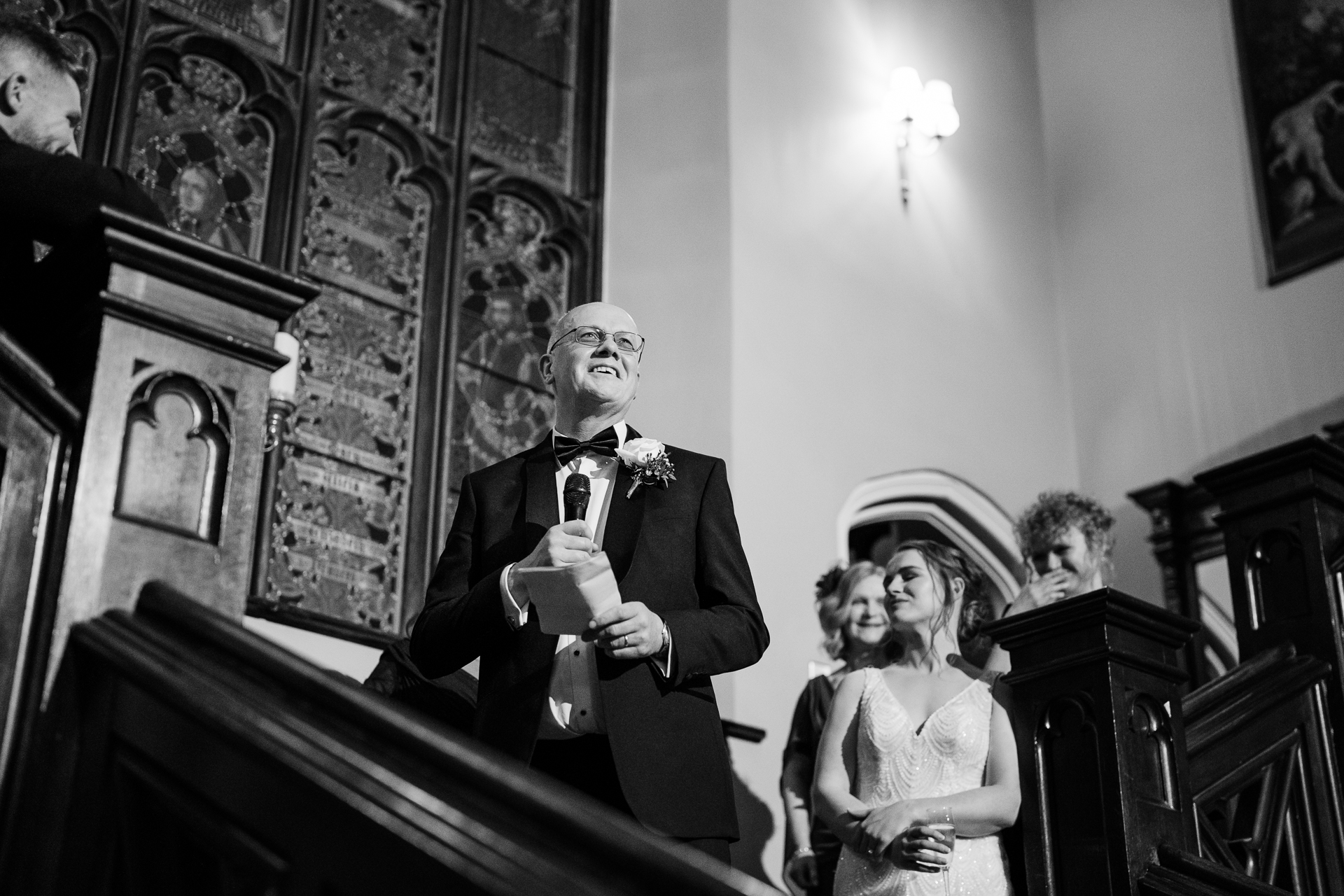 A person in a tuxedo speaking into a microphone in front of a group of people