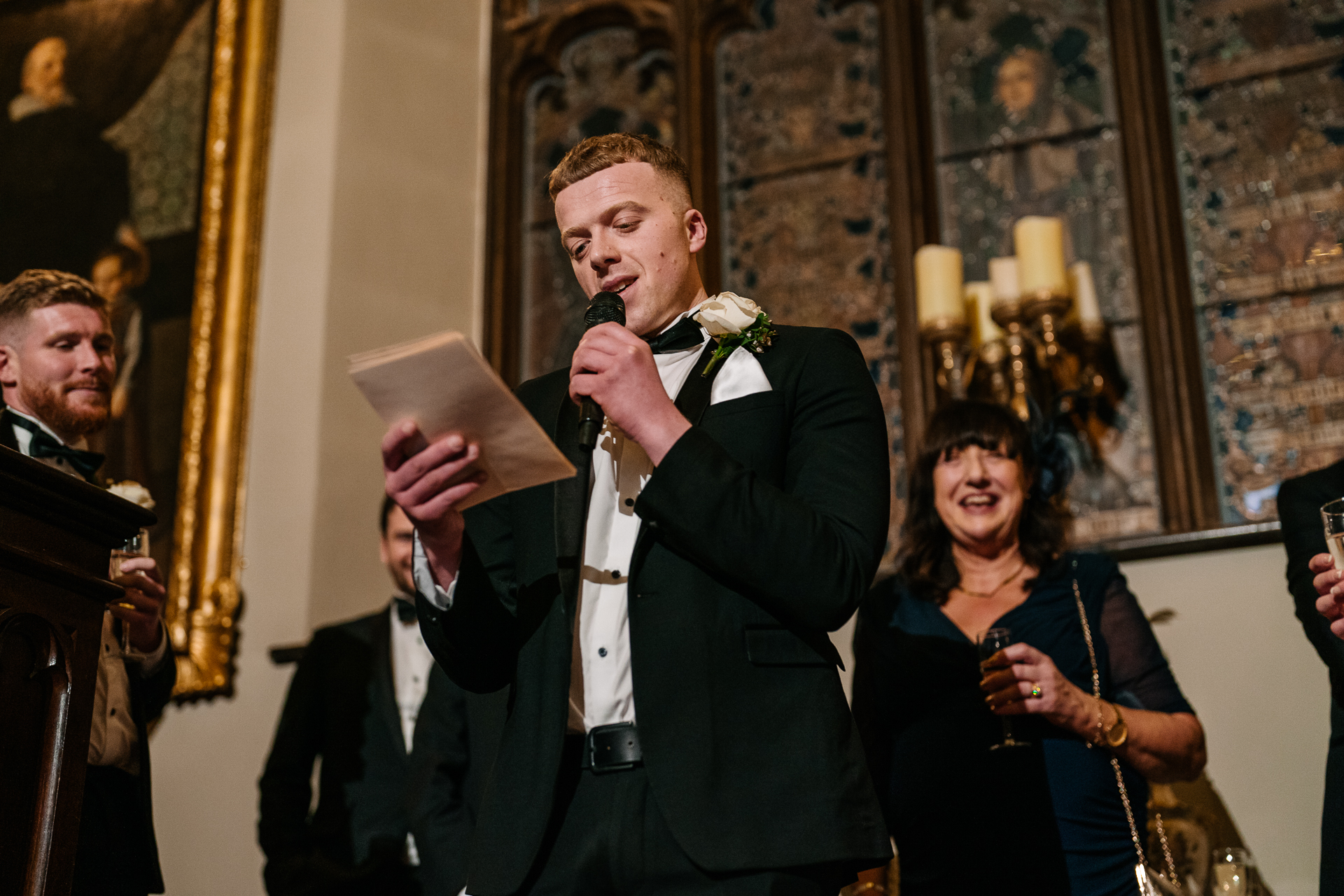 A person in a suit holding a microphone and a paper in front of a group of people