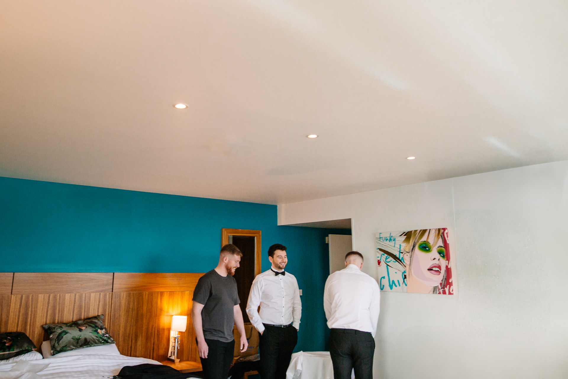 A group of men standing in a room with a bed and a lamp