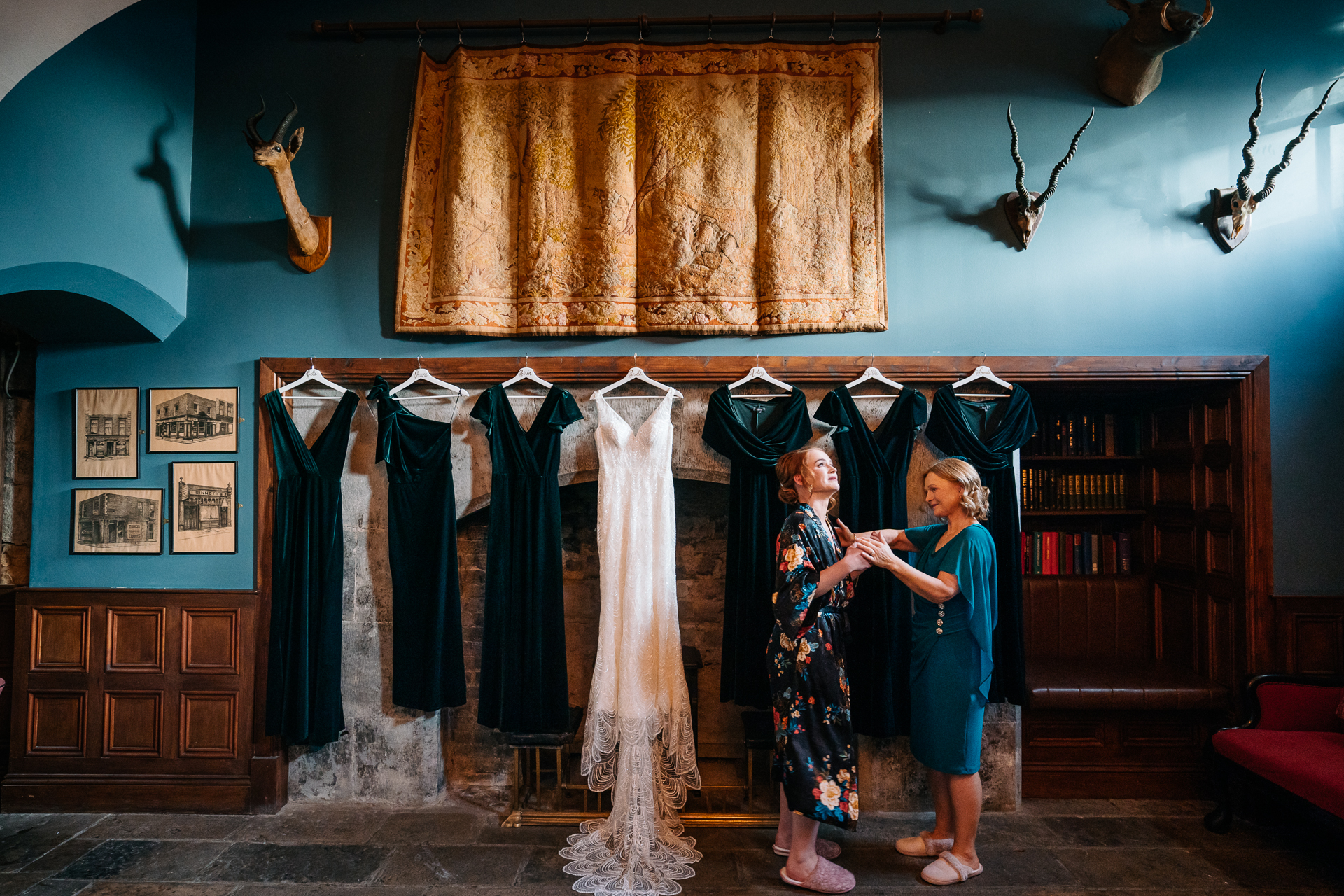 A couple of women in dresses standing in front of a stage with a curtain and a bookcase