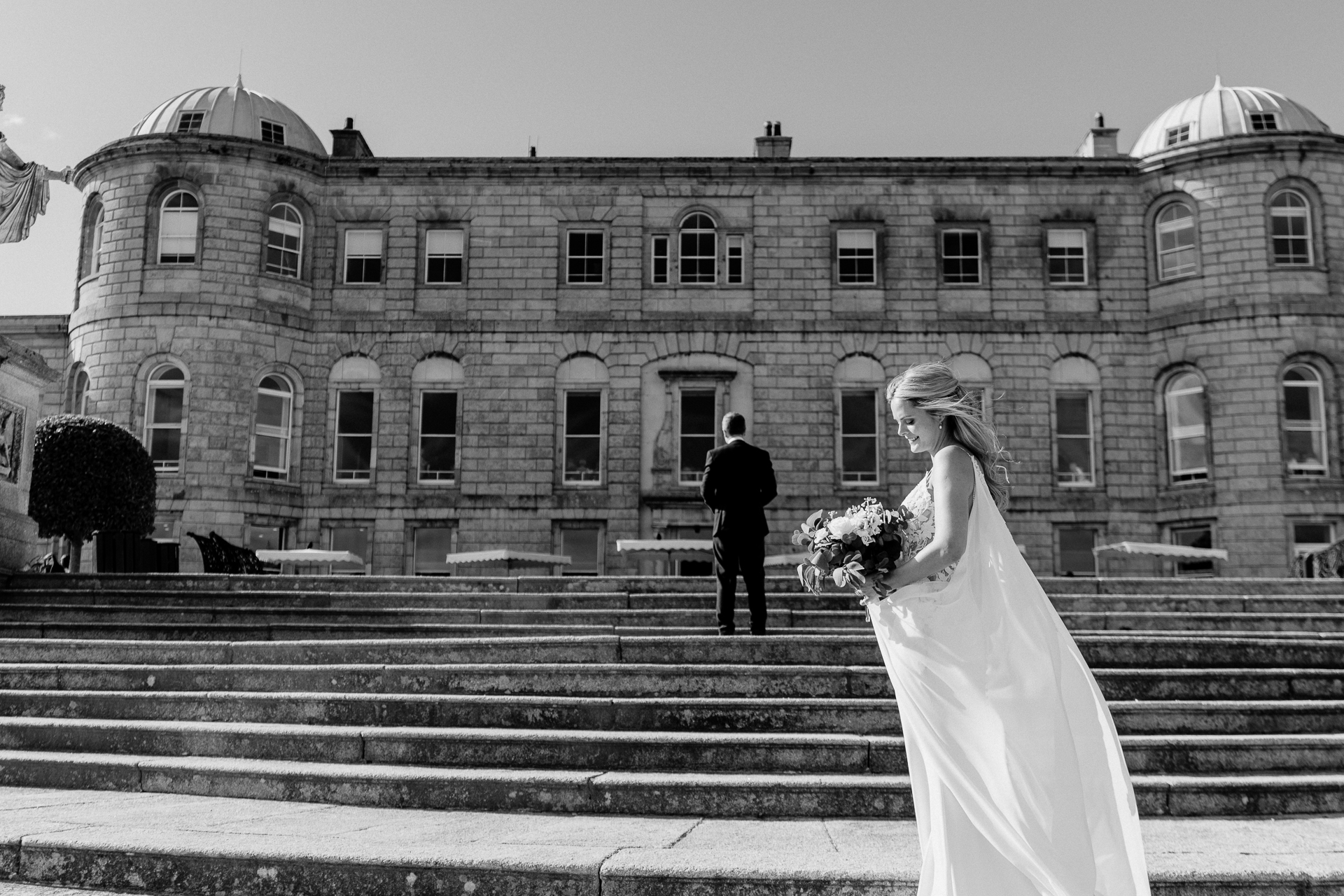 A bride and groom on stairs in front of a large building