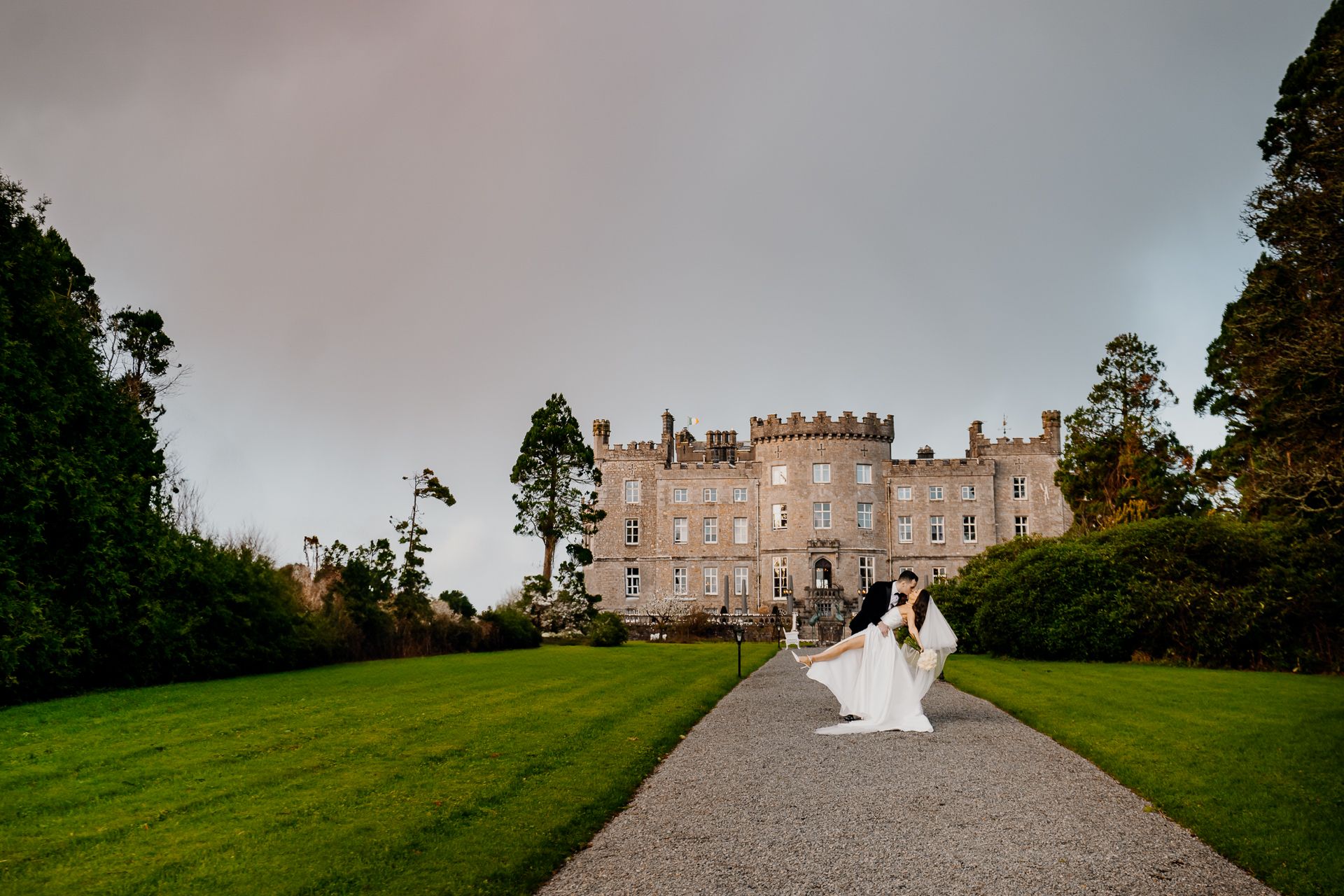 A man and woman in wedding attire walking down a path in front of a large building