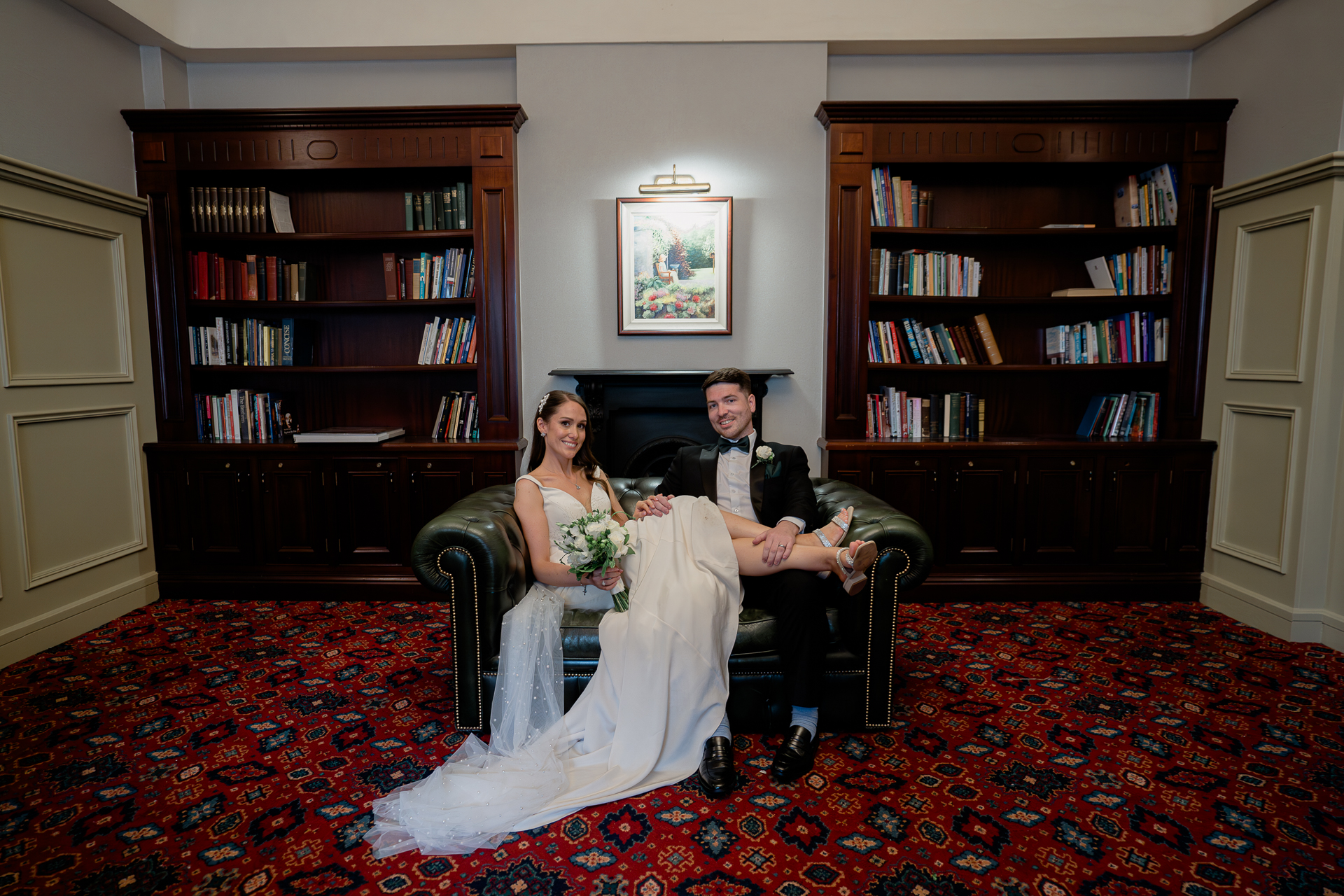 A man and woman sitting on a couch in a room with a bookcase and a book shelf