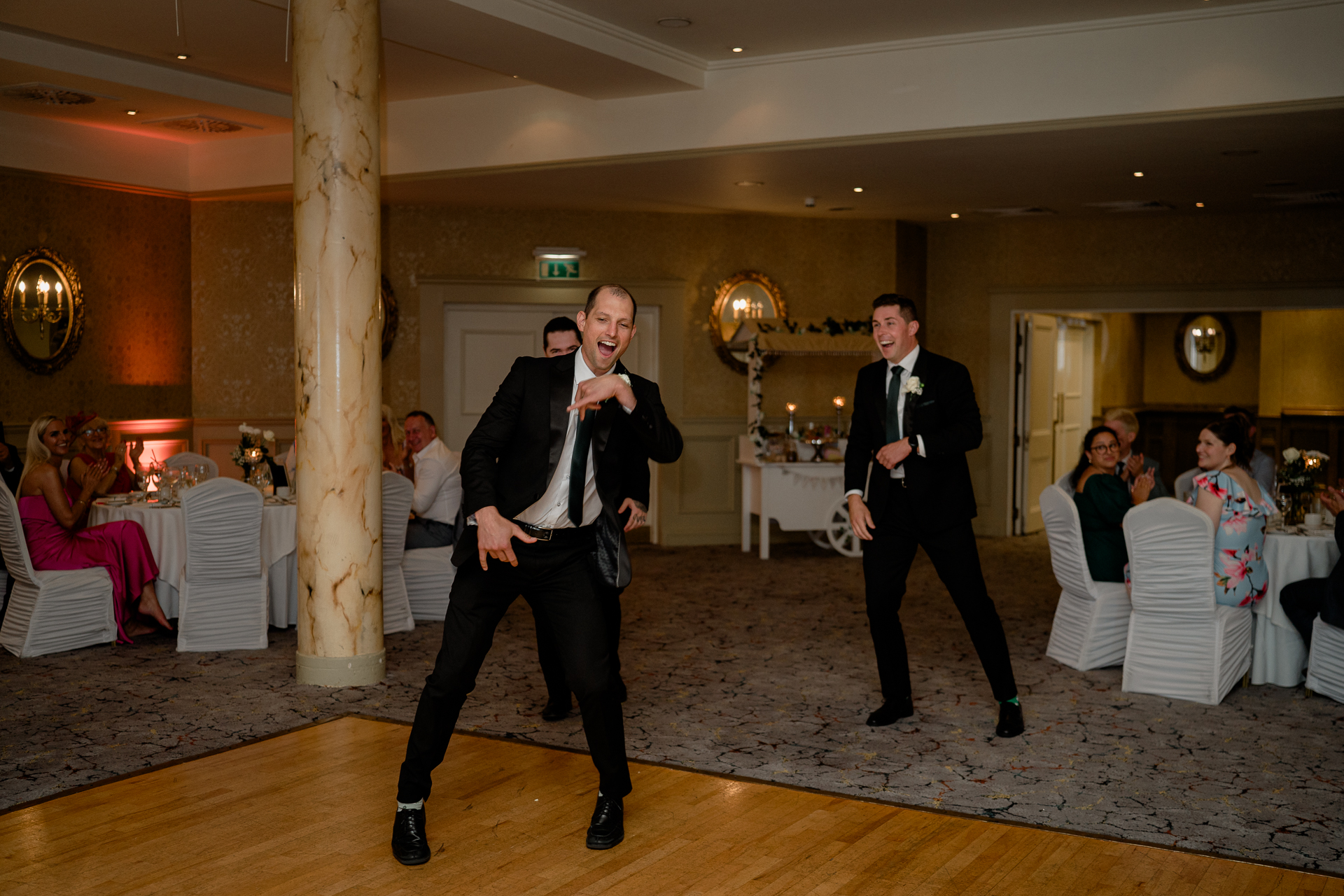 A couple of men dancing in a room with people in the back