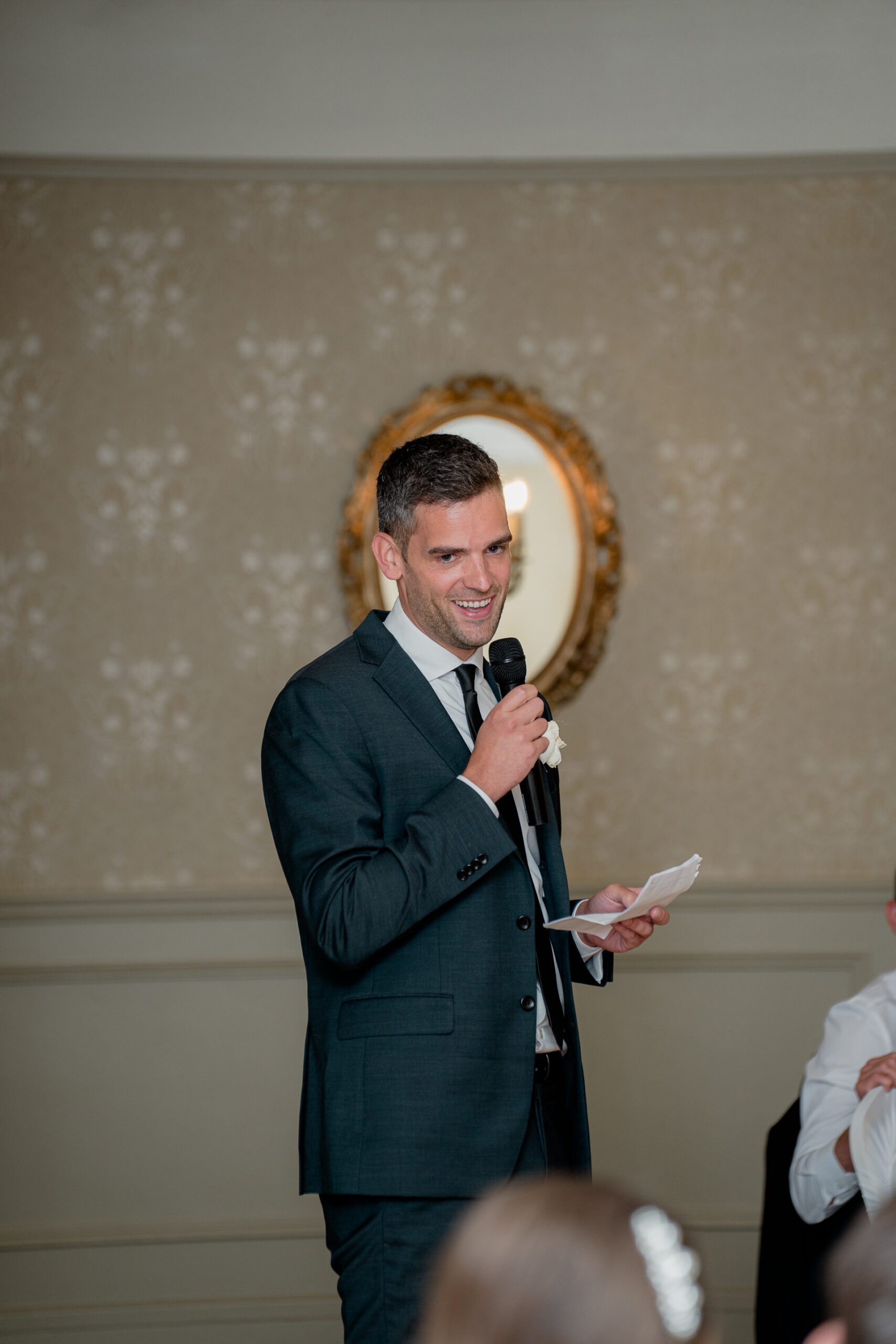 A person in a suit holding a microphone and a paper