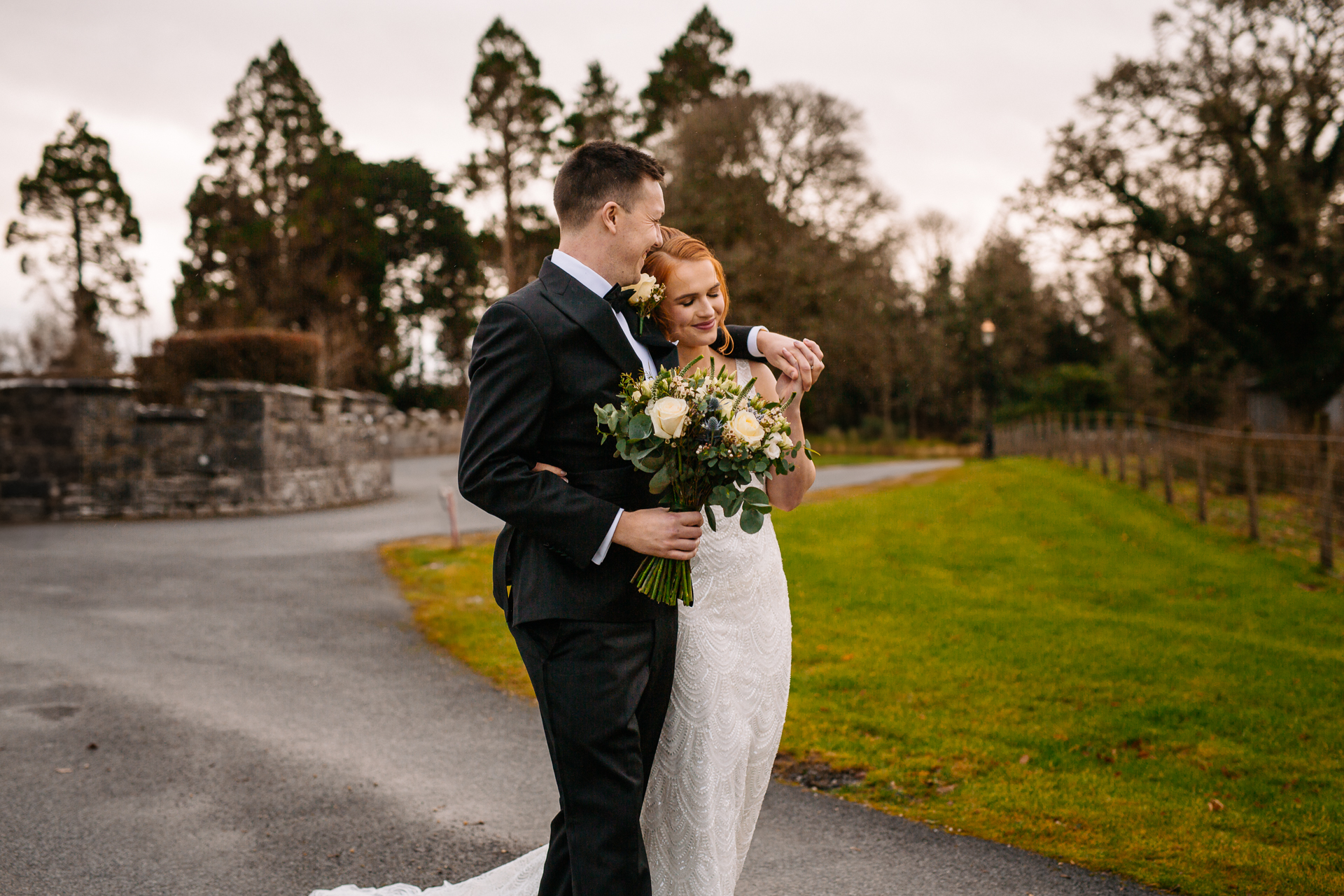 A man and woman kissing on a road with grass and trees