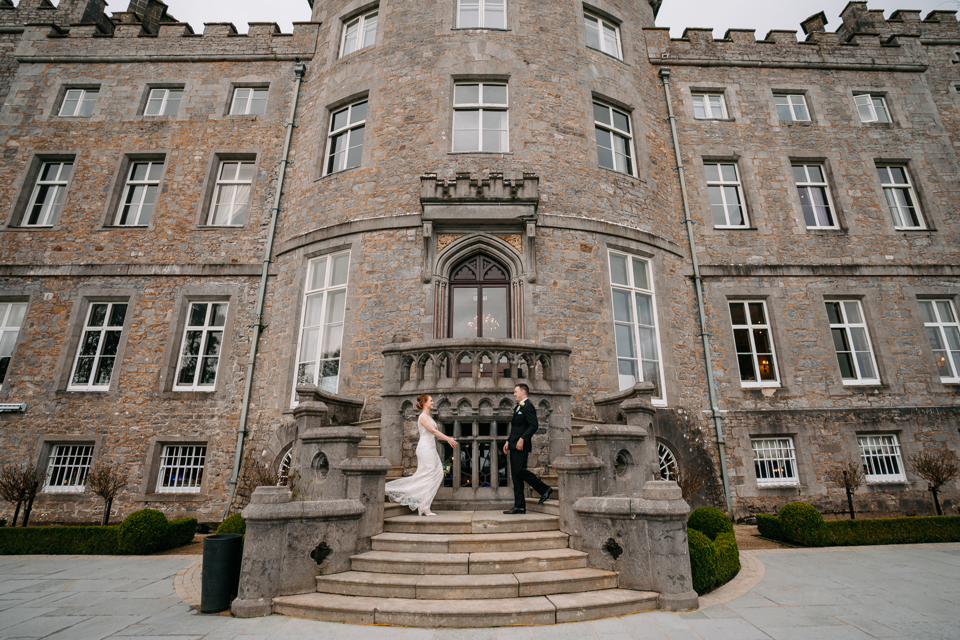 A bride and groom on steps in front of a large brick building