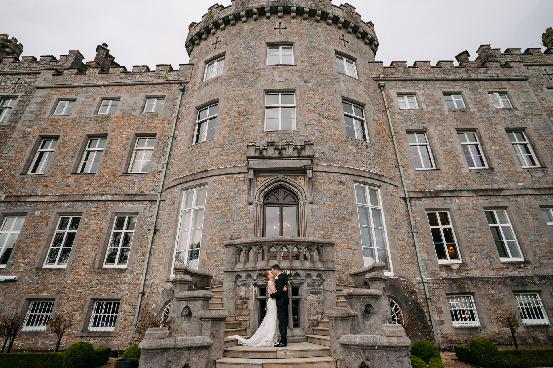 A bride and groom kissing in front of a large brick building