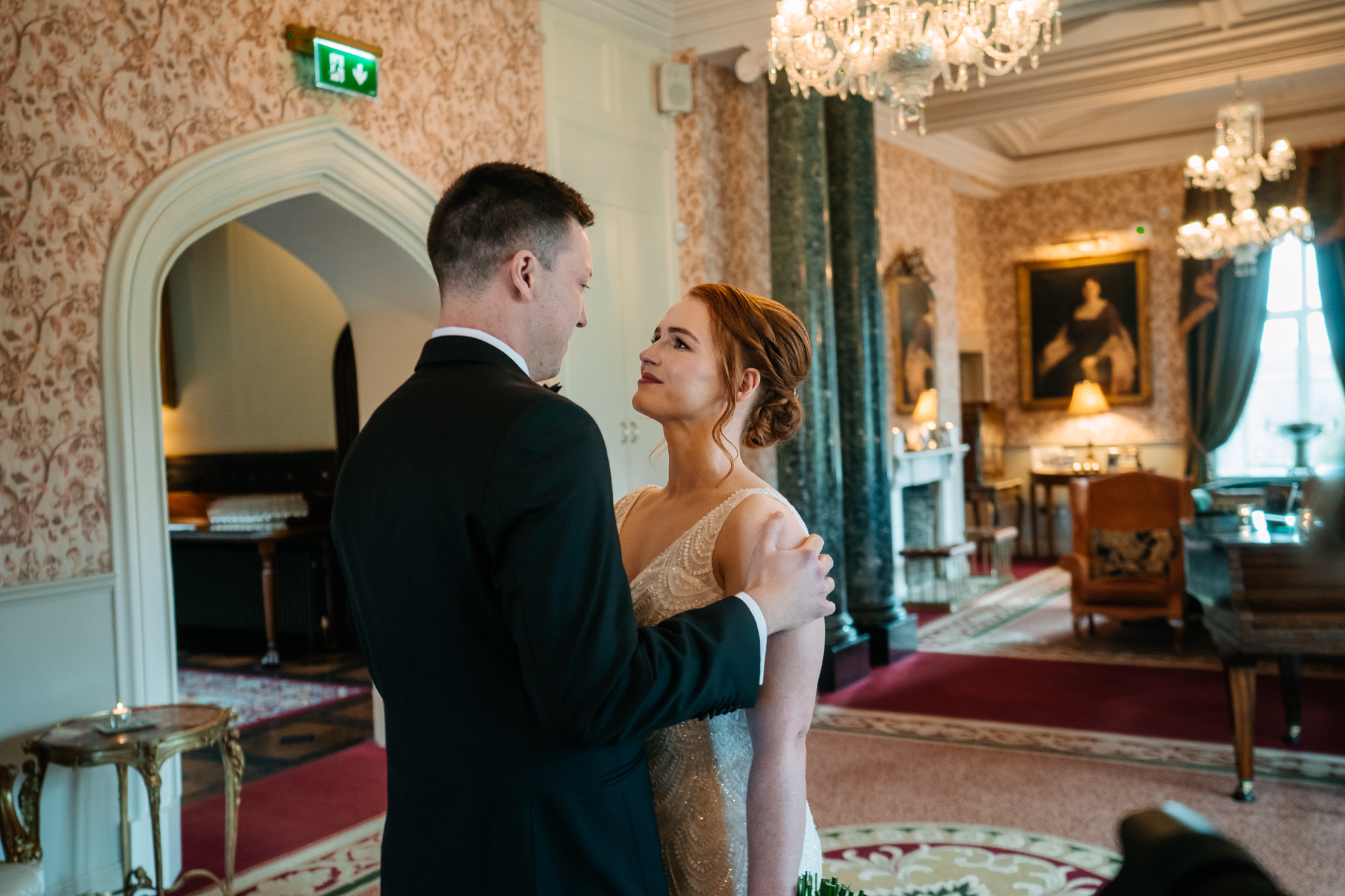 A man and woman kissing in a room with chandeliers and a piano