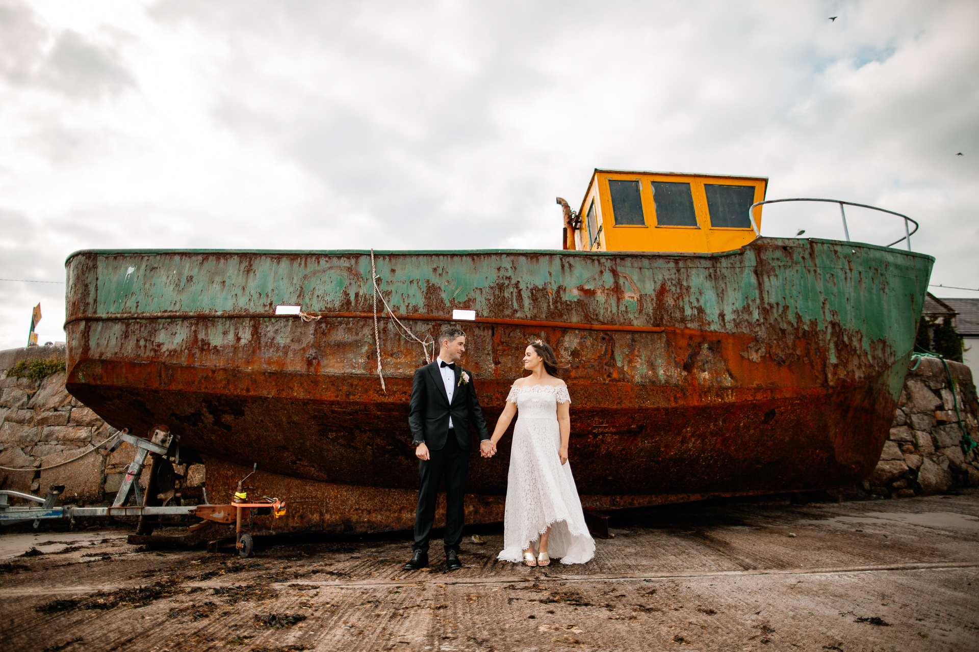 A bride and groom standing in front of a rusted boat