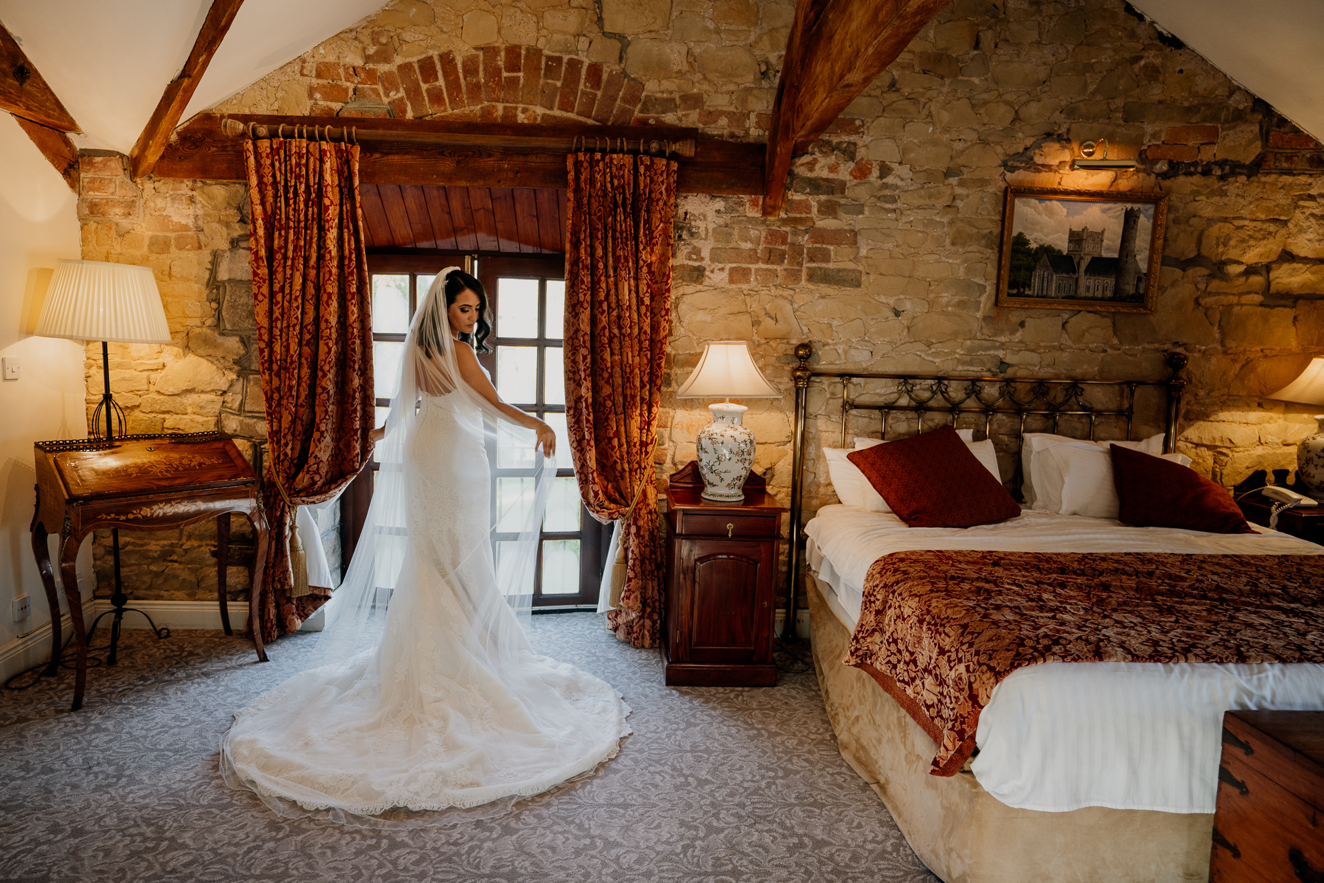 A bride in a stunning wedding gown stands in a luxurious Cabra Castle suite, capturing an intimate pre-wedding moment.