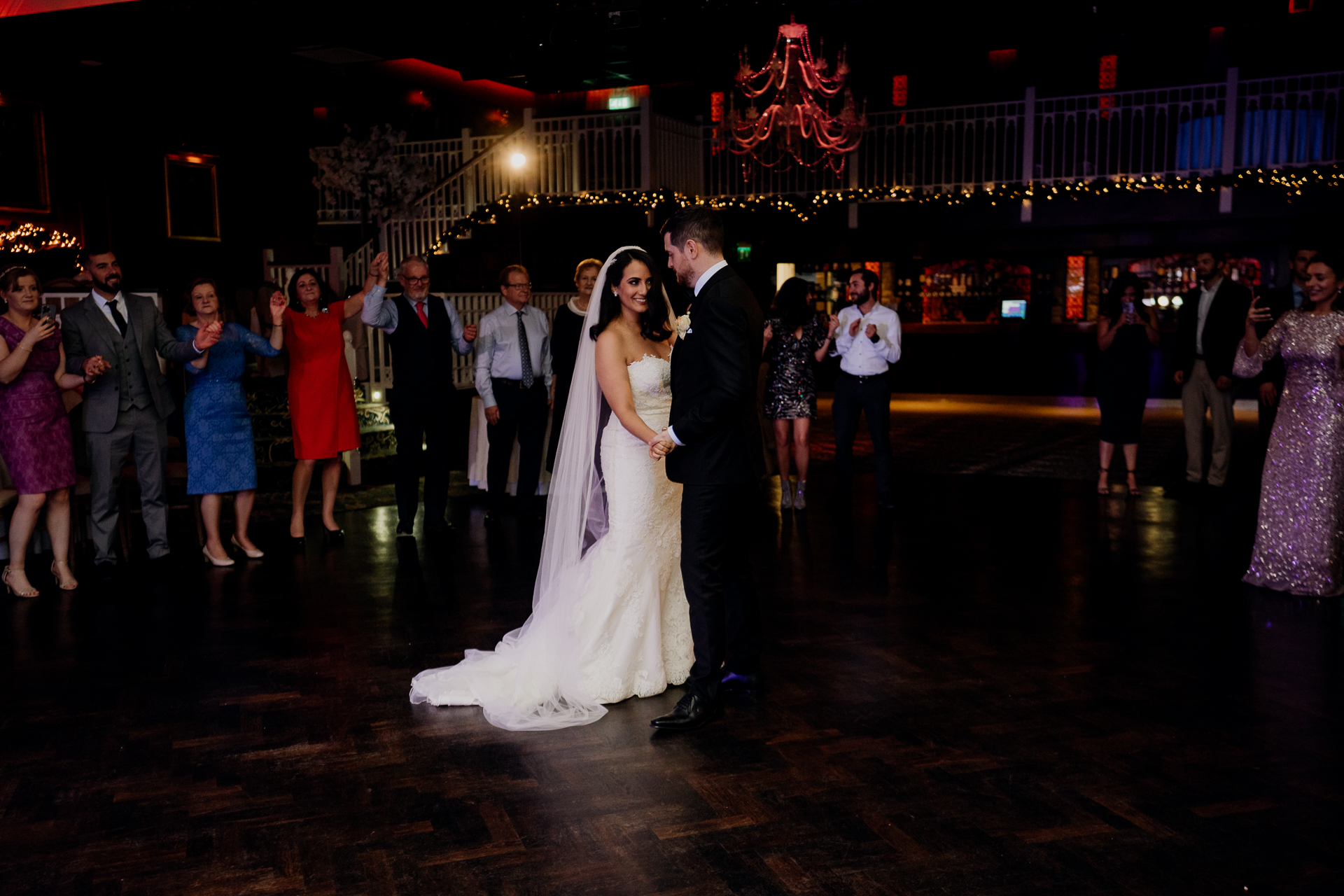 A newlywed couple shares their first dance at Cabra Castle, surrounded by dim romantic lighting and their loved ones.