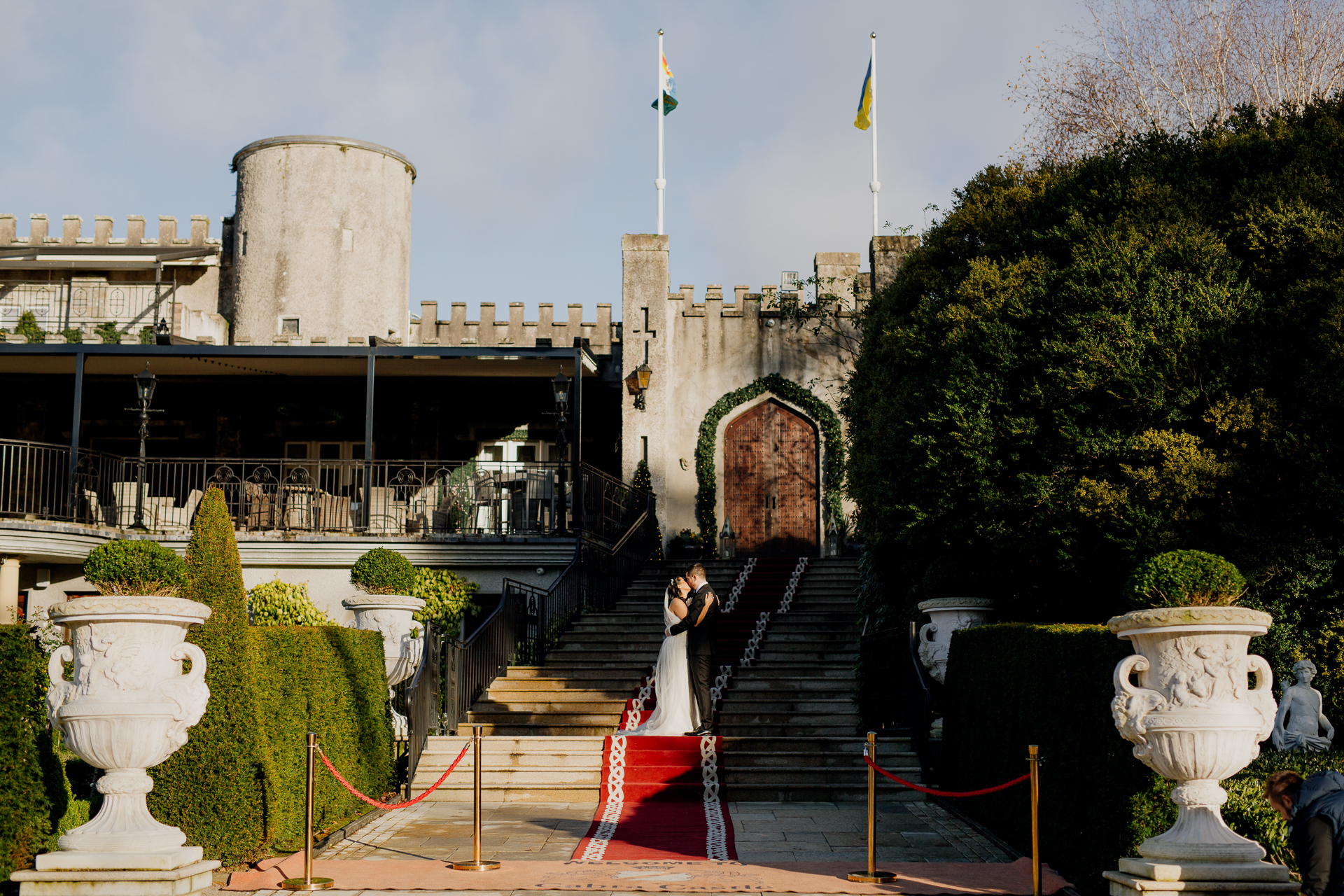 A newlywed couple standing in front of the grand entrance of Cabra Castle, framed by elegant gardens and historic architecture.