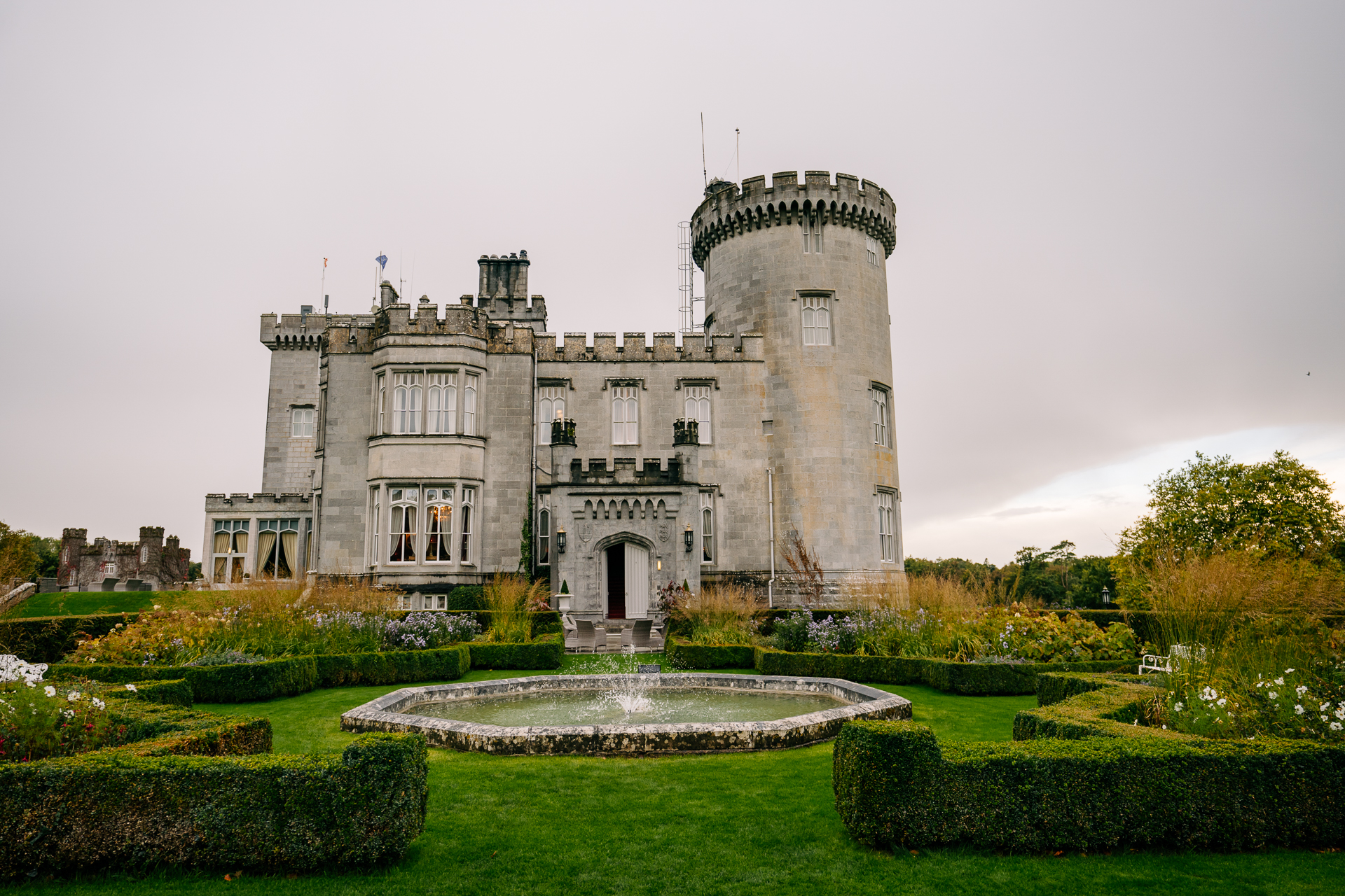 A large stone building with a fountain in front of it with Dromoland Castle in the background