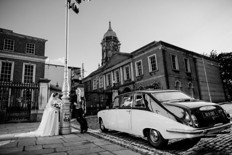 Bride and groom sharing a candid moment next to a vintage car in Dublin city – captured by a Dublin Wedding Photographer