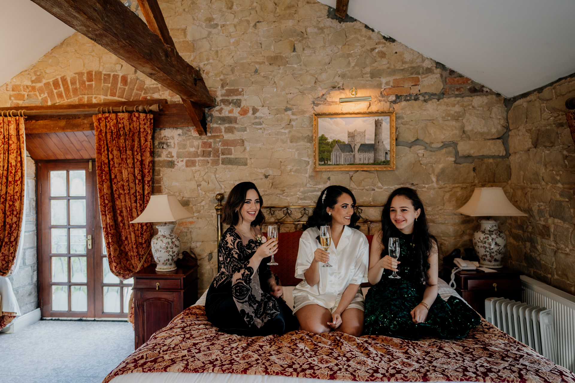 Bridesmaids sitting together on a bed in the bridal suite at Cabra Castle, during the morning preparations.