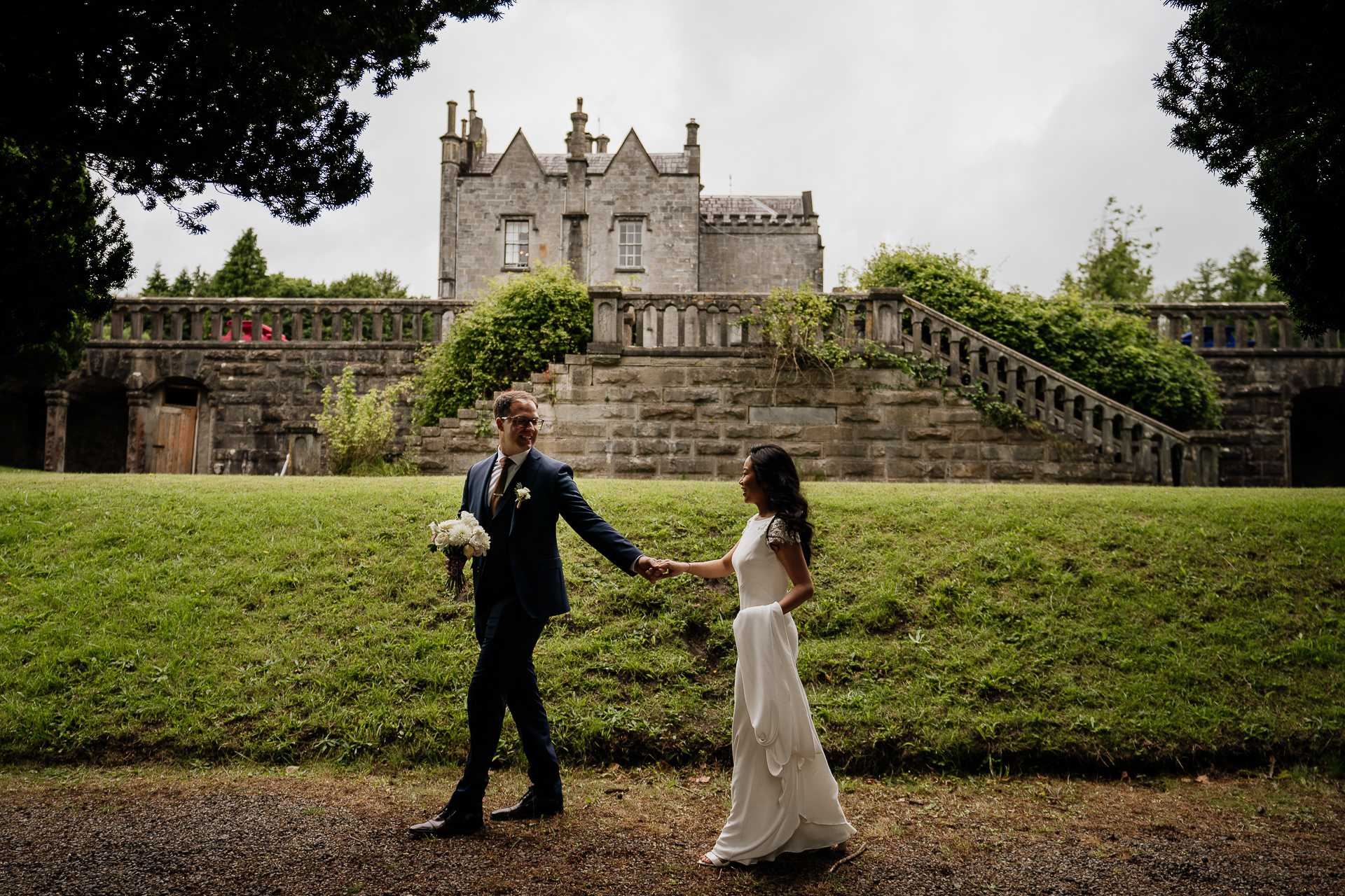 Bride and groom walking hand in hand on Belleek Castle front lawn with castle backdrop