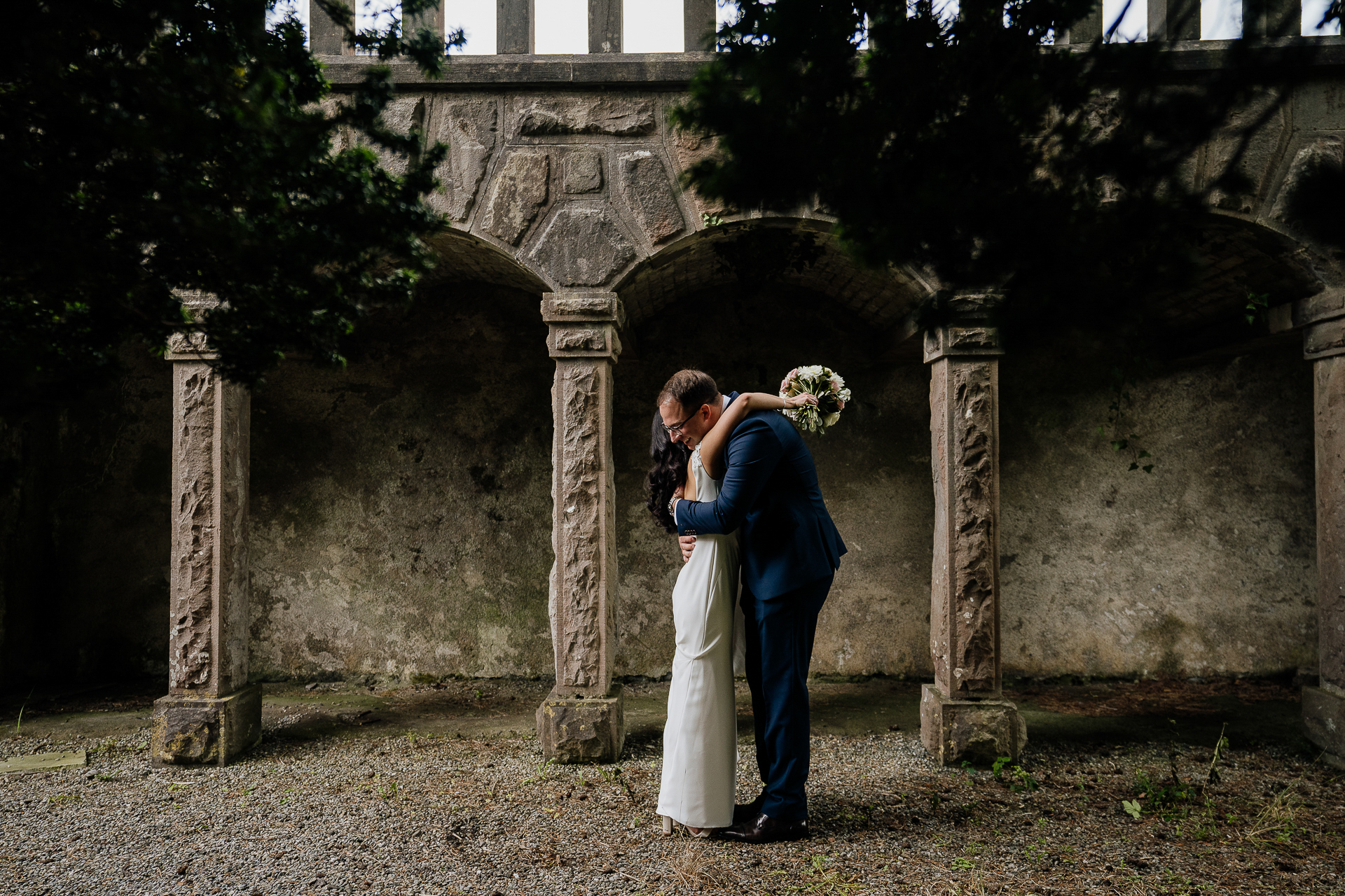 bride and groom embrace during first look at belleek castle under stone arches