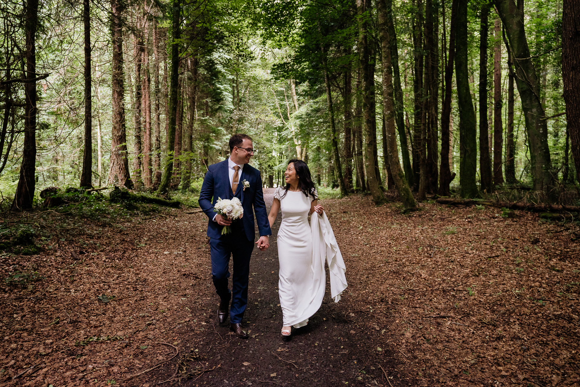 Bride and groom walking hand in hand along forest path at Belleek Castle