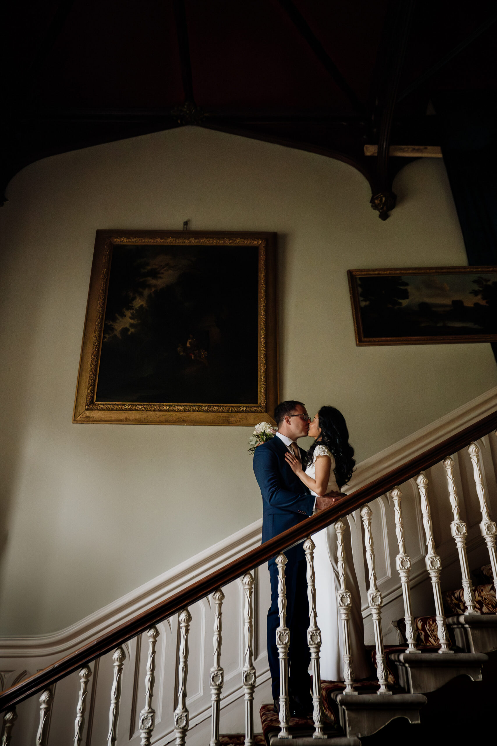 Bride and groom embrace on a staircase under a moody chandelier light at Belleek Castle