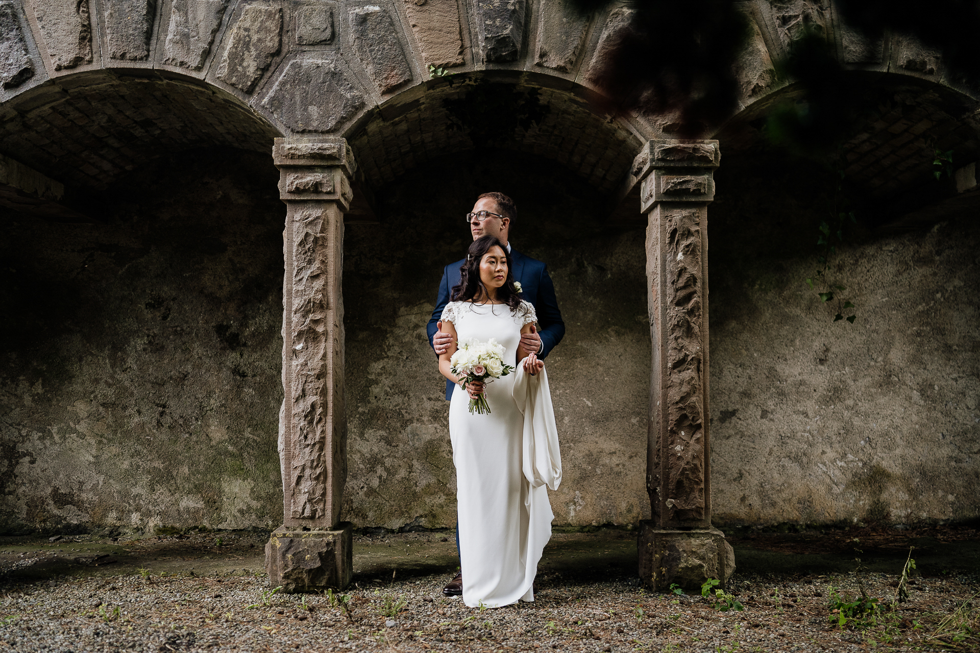 Bride standing under the hidden archway at Belleek Castle, holding a bouquet and posing for an elegant portrait.