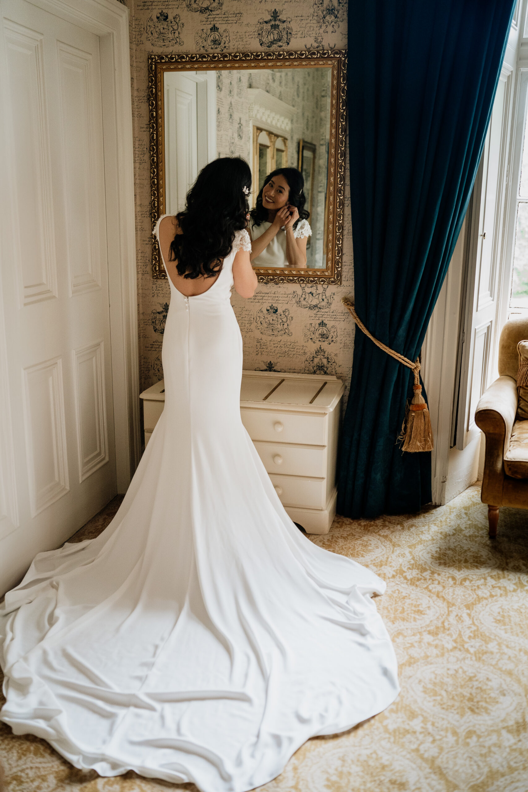 The bride looking in the mirror while adjusting her dress in a bright room at Belleek Castle