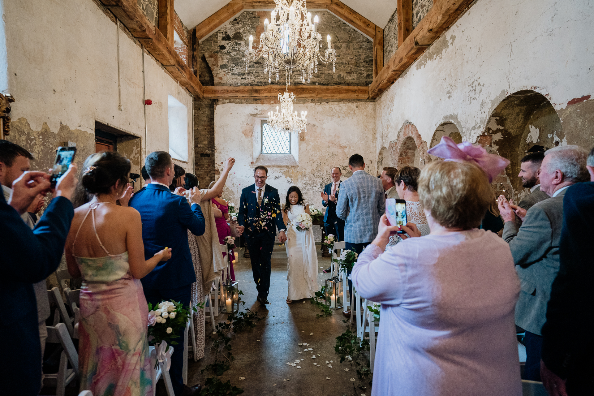 The newlyweds walking down the aisle together at Belleek Castle while guests cheer and take photos