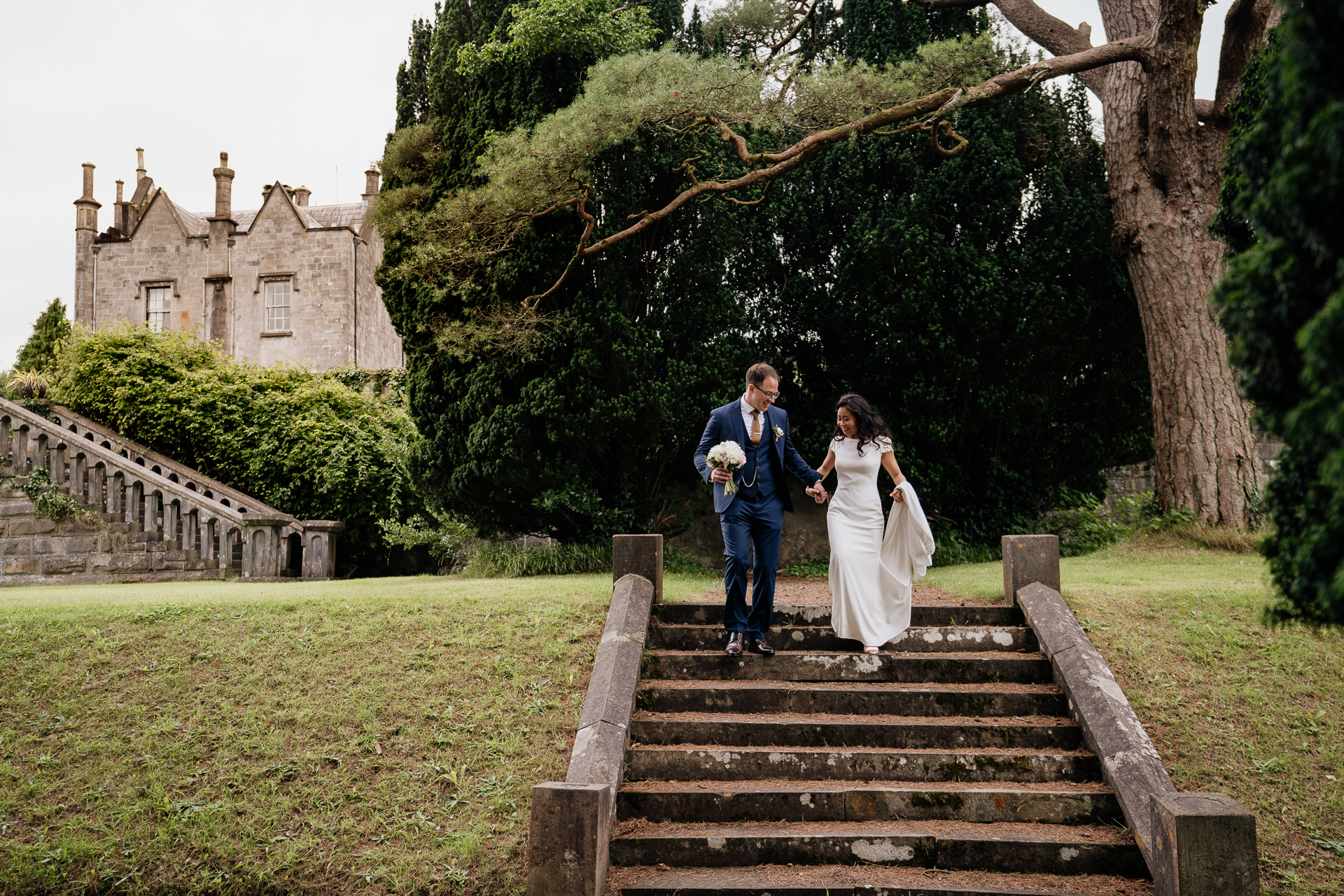 Bride and groom walking down outdoor stone steps at Belleek Castle, holding hands