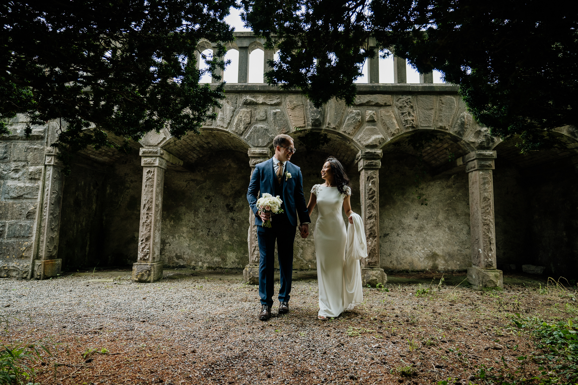 Bride and groom holding hands in front of old stone arches at Belleek Castle