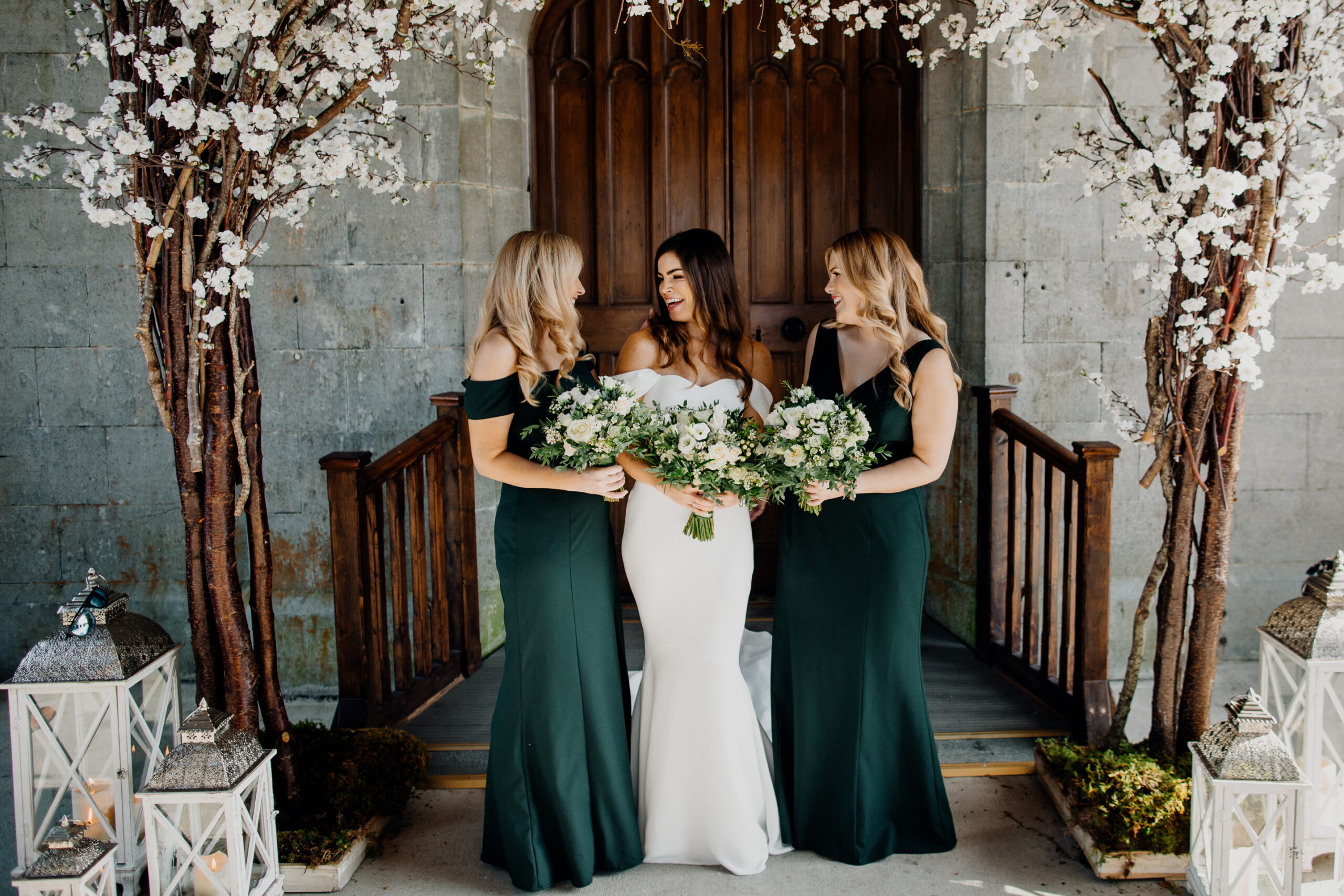 Bride and bridesmaids laughing together under spring blossoms at Markree Castle – perfect moment from a destination wedding in Ireland.