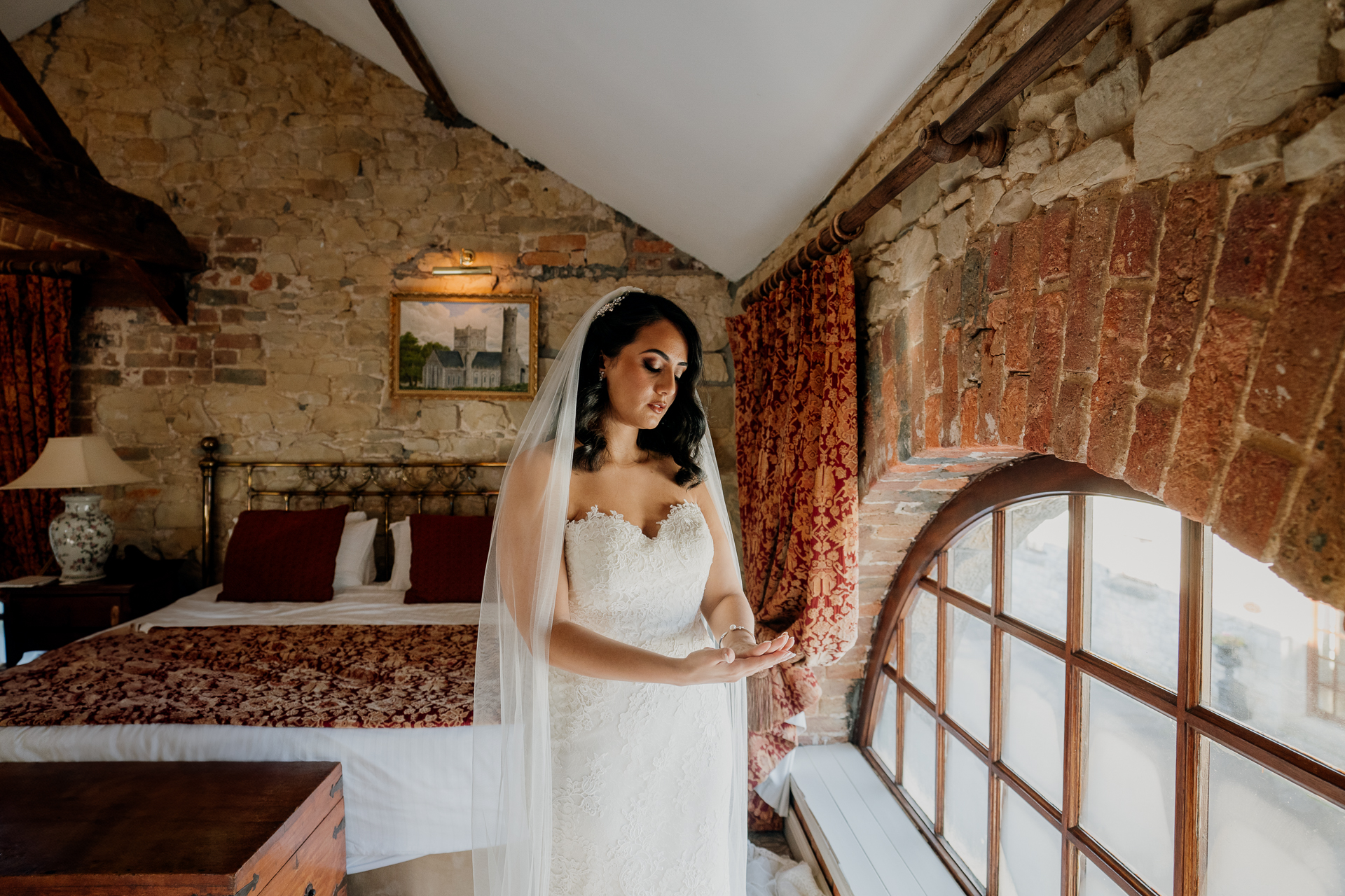 Bride getting ready in a stone room at Cabra Castle, standing by a curved window.