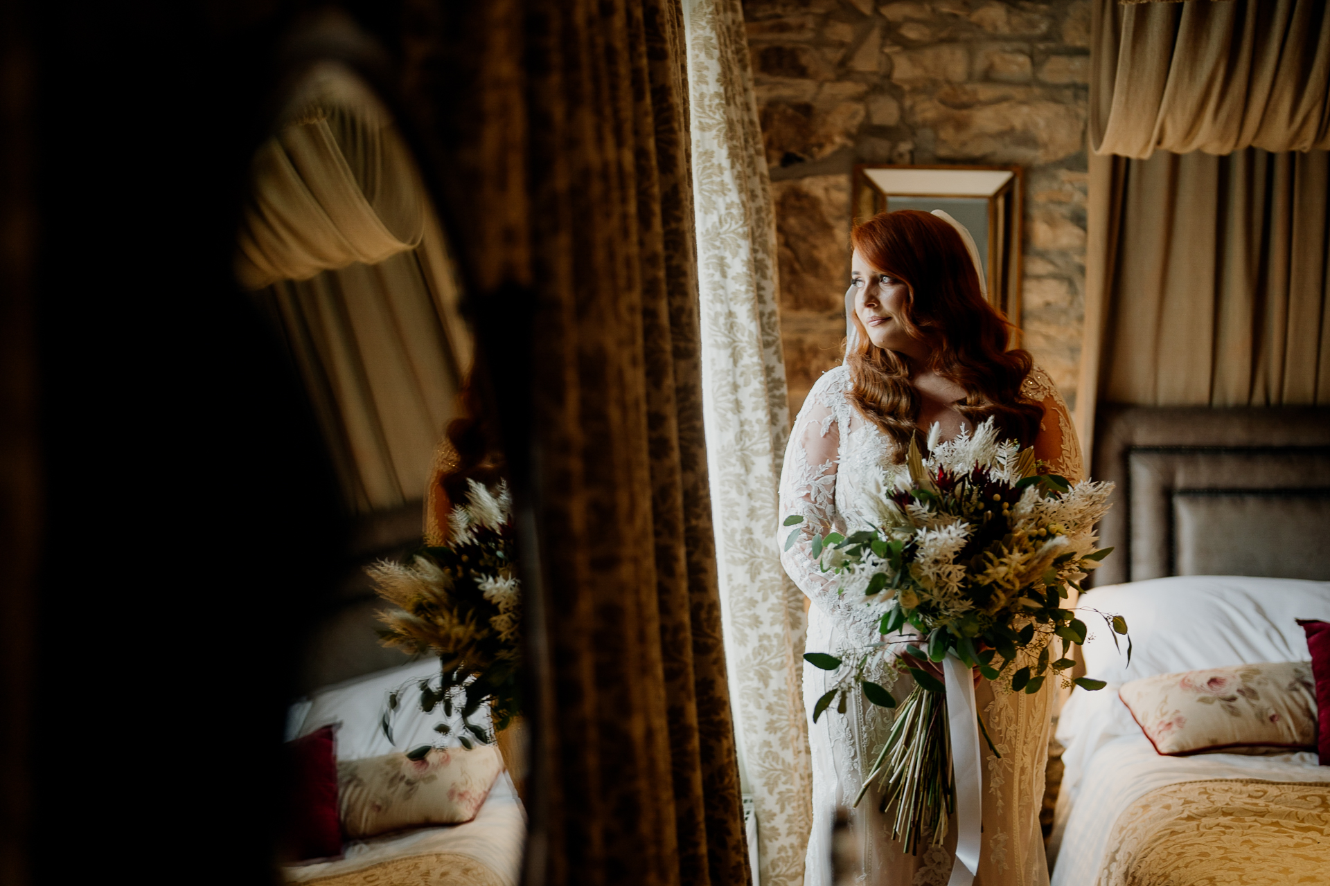 Bride standing by a window at Cabra Castle, holding a bouquet and bathed in soft natural light.