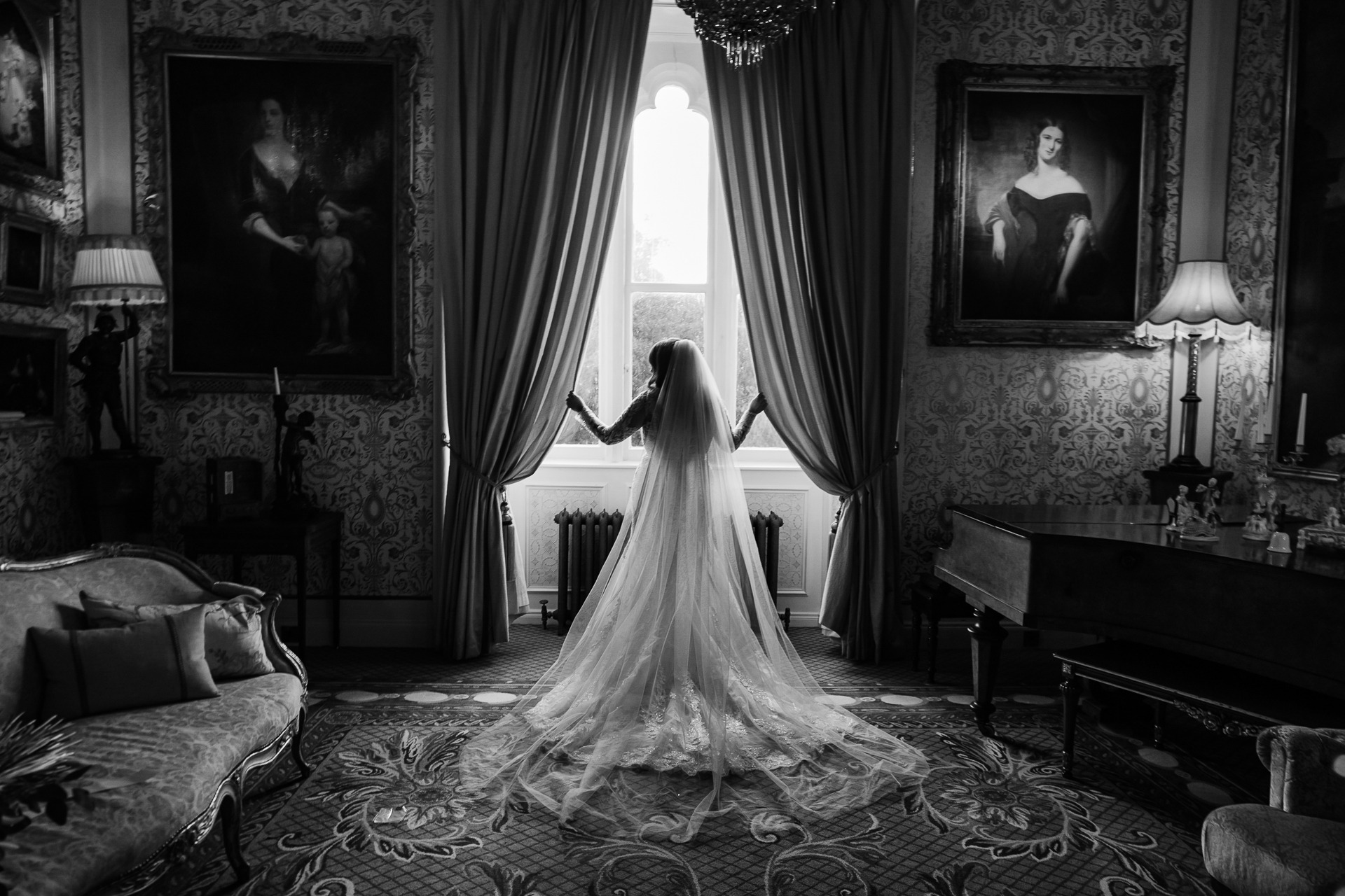 Bride in wedding dress looking out the window at Cabra Castle, captured in black and white.