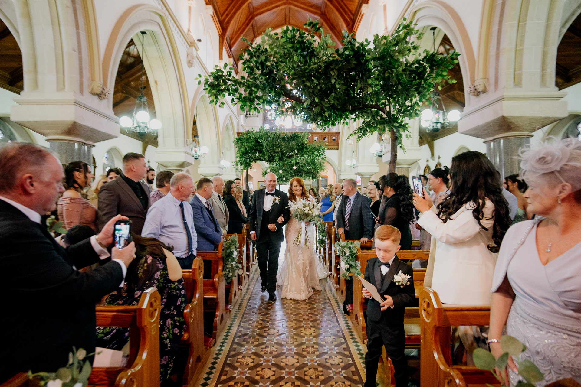 Bride walking down the aisle in a beautifully decorated church at Cabra Castle, with guests watching.