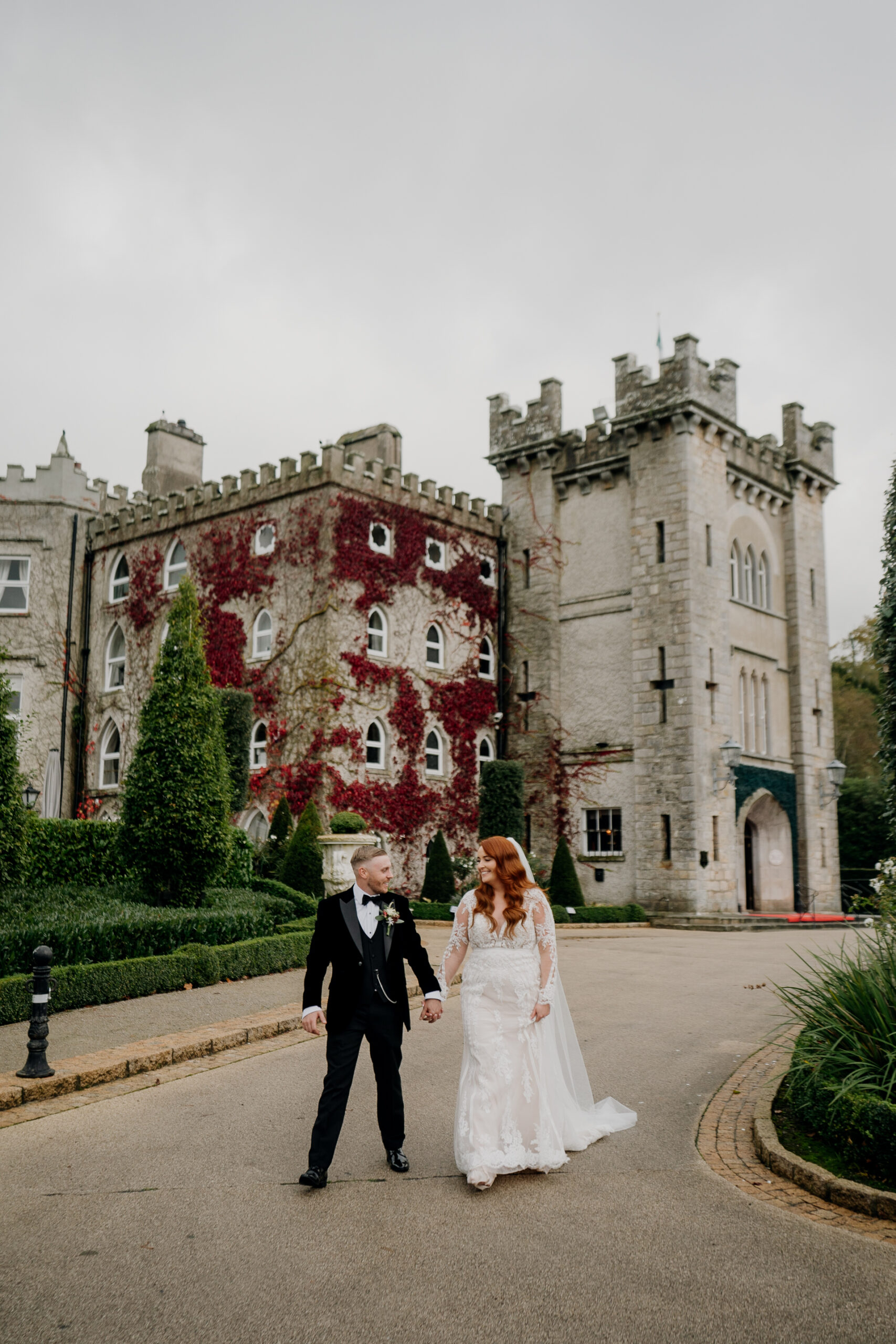 Bride and groom walking hand in hand by red ivy wall at Cabra Castle