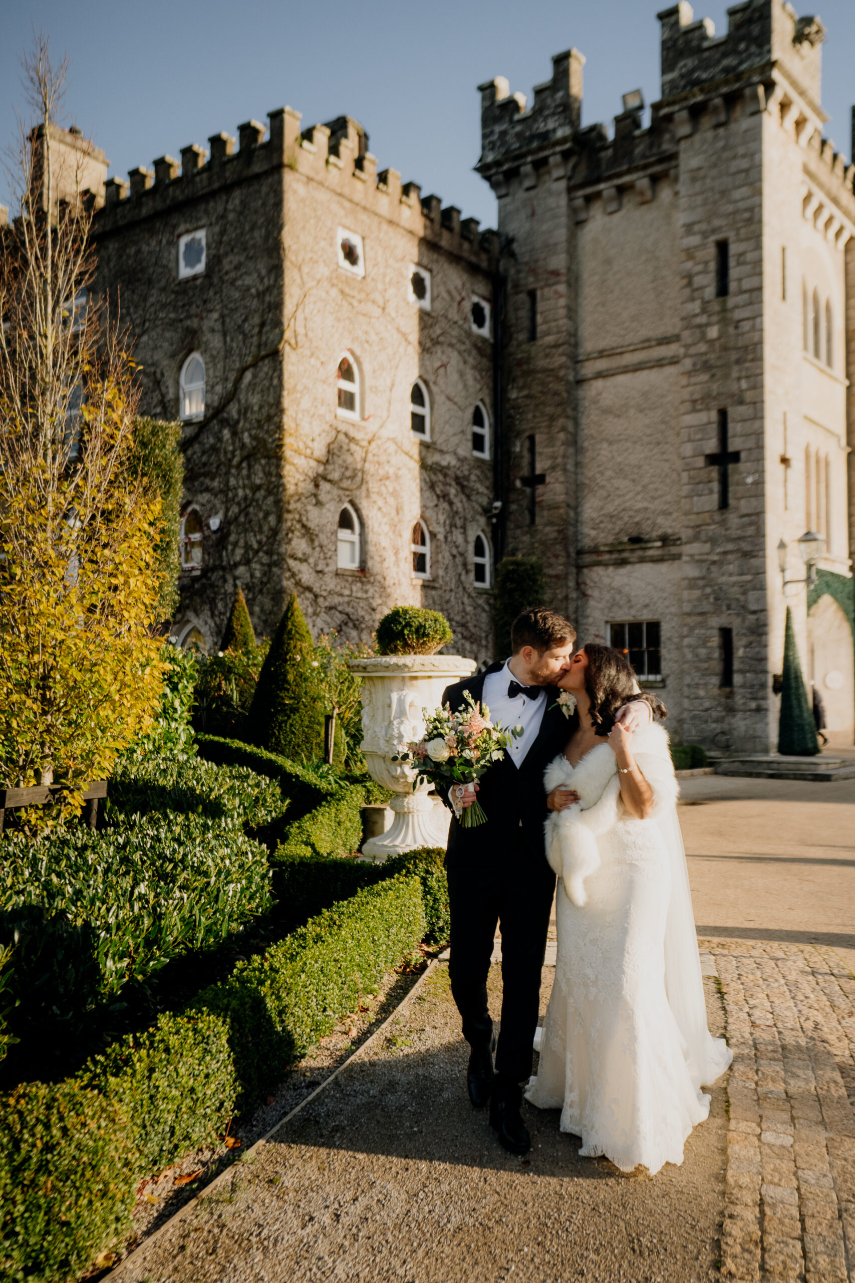 A bride and groom kissing on a garden path with Cabra Castle in the background