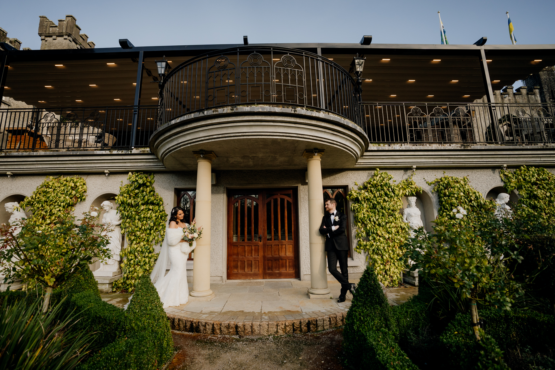 Bride and groom standing together in front of the columned entrance and balcony of Cabra Castle, captured during their wedding day.