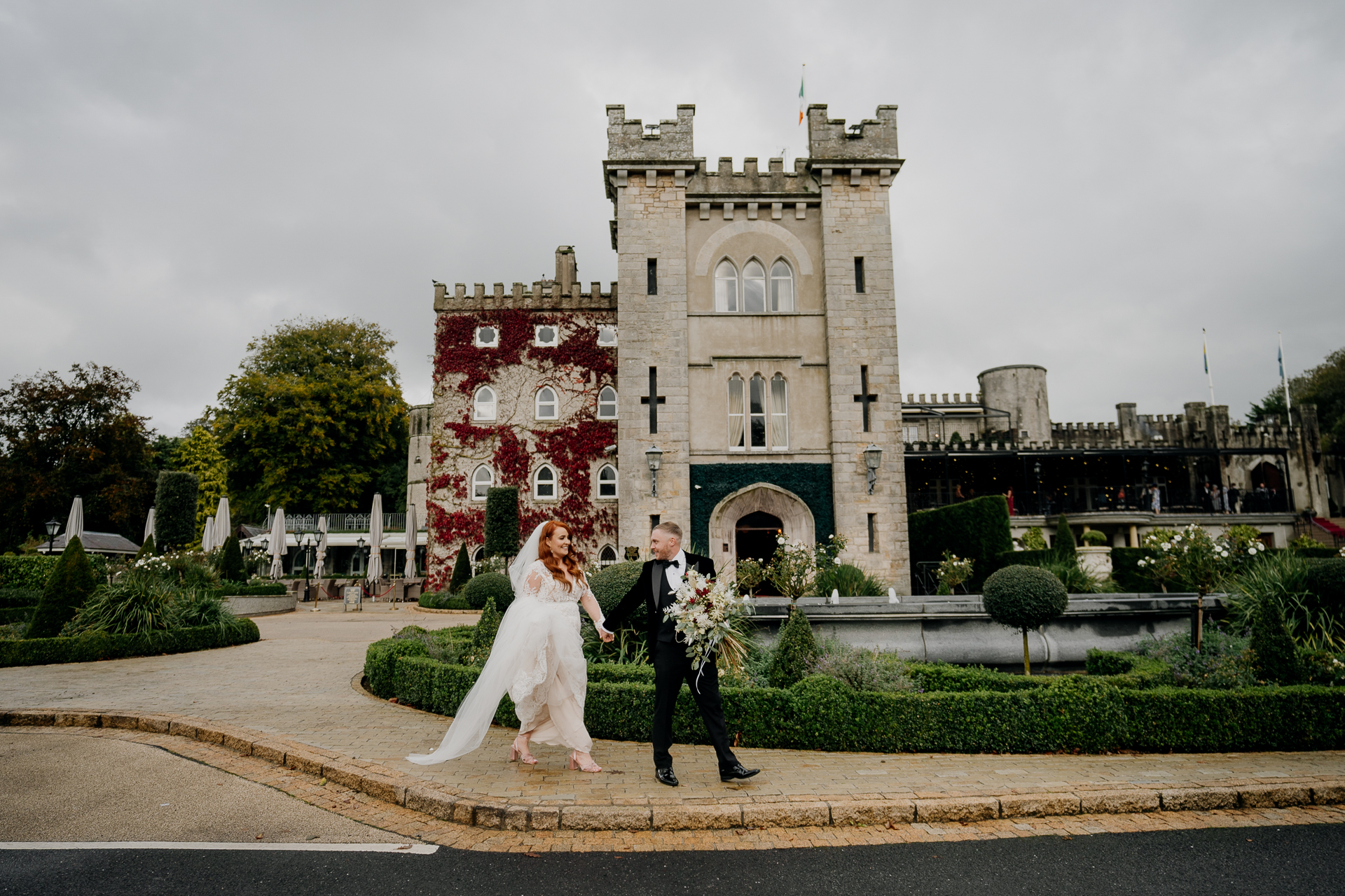 Bride and groom walking hand in hand in front of Cabra Castle on their wedding day