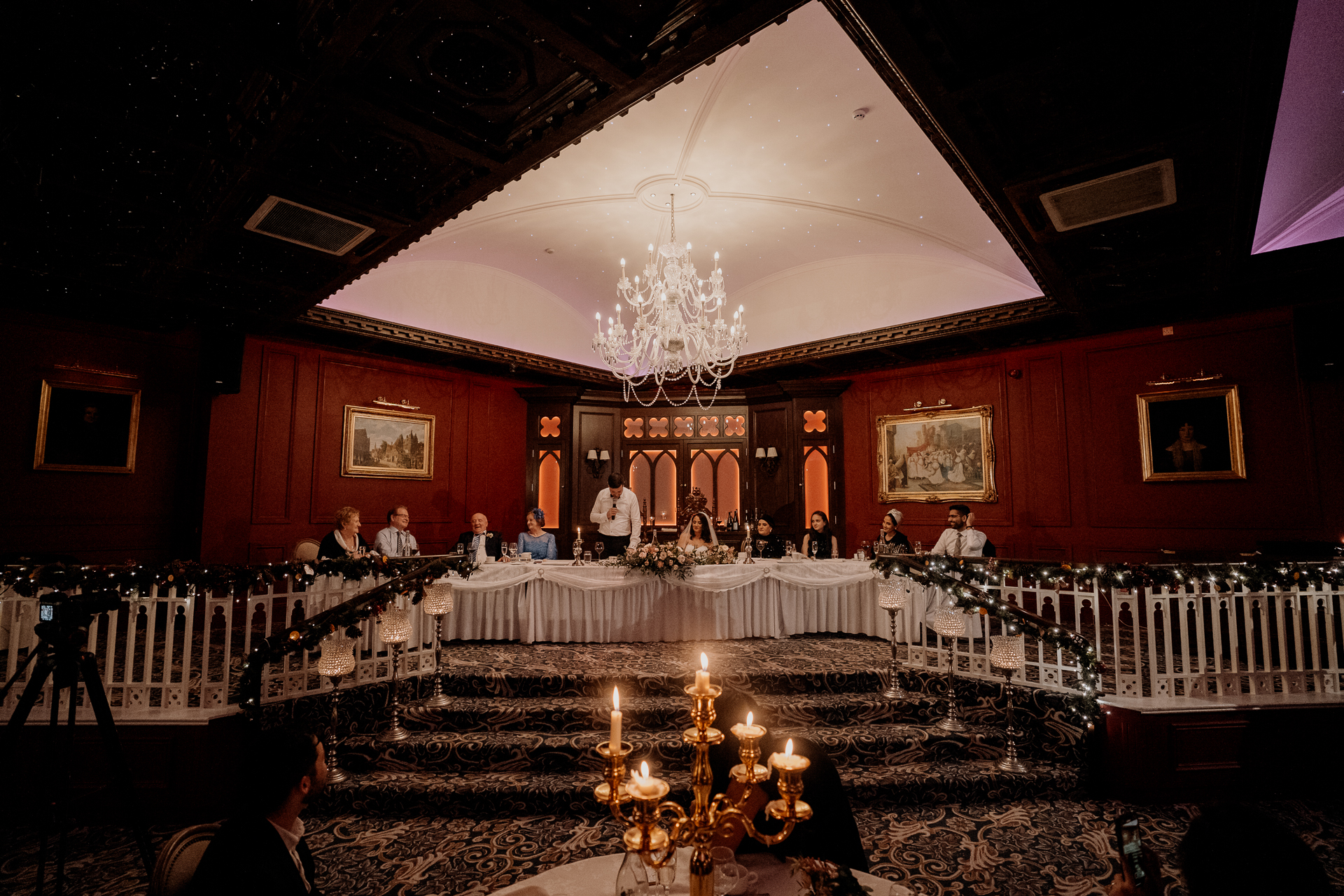 Wedding speeches at the top table during an evening reception at Cabra Castle, with elegant lighting and vintage decor