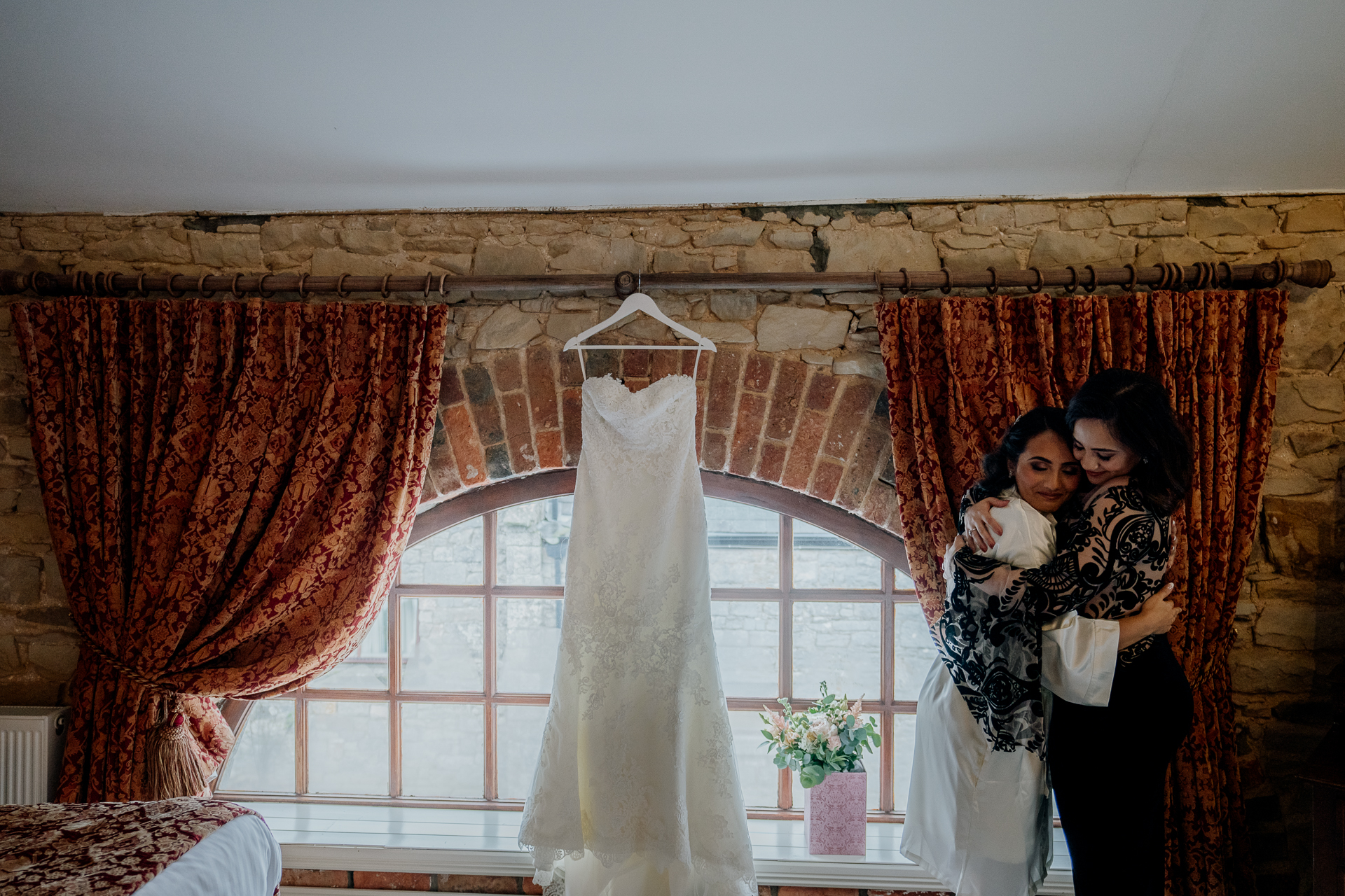 Wedding dress hanging between two red curtains with a bridesmaid holding a baby beside it – Cabra Castle Wedding Morning