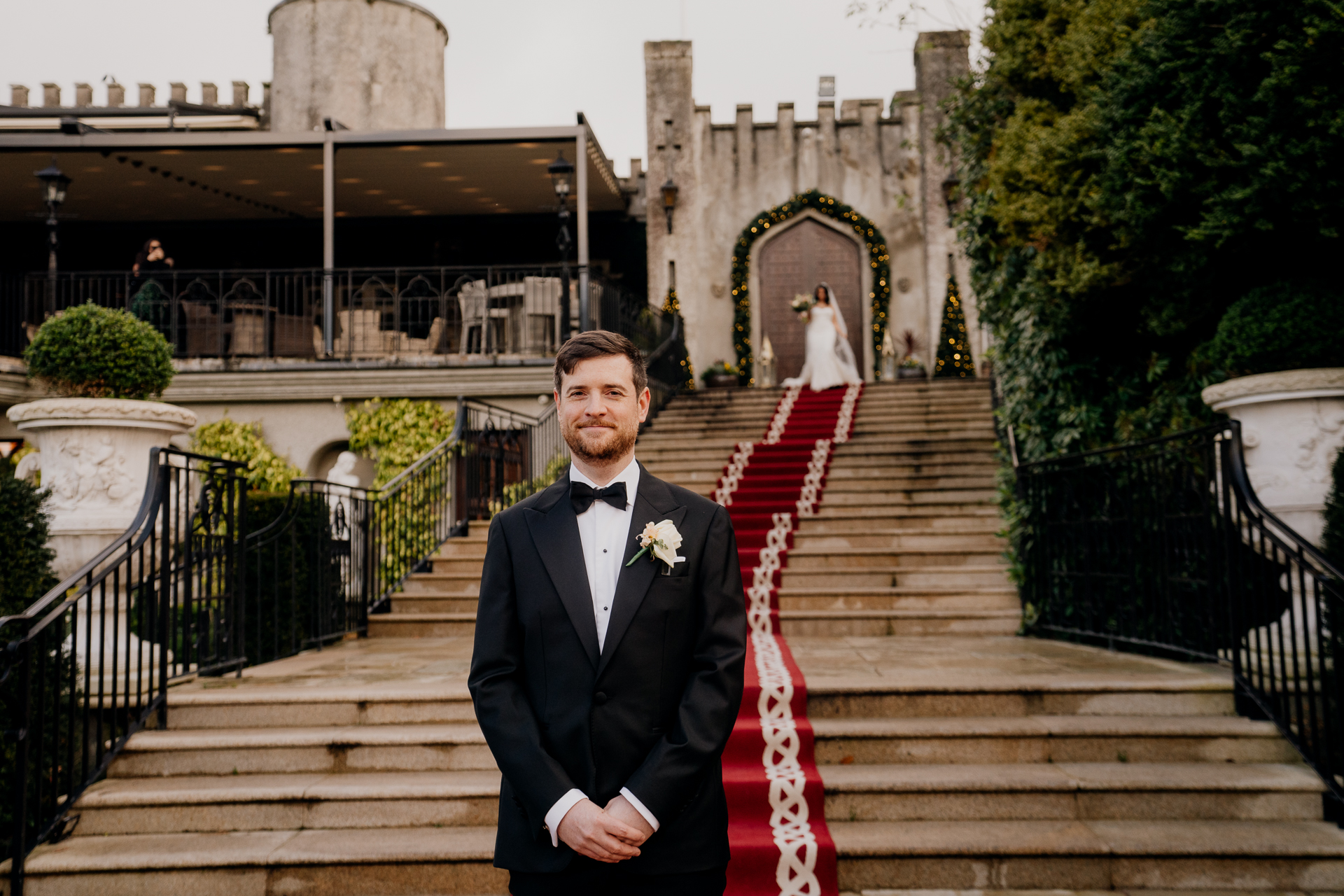 Groom waiting on the grand red-carpeted staircase at Cabra Castle for the first look moment